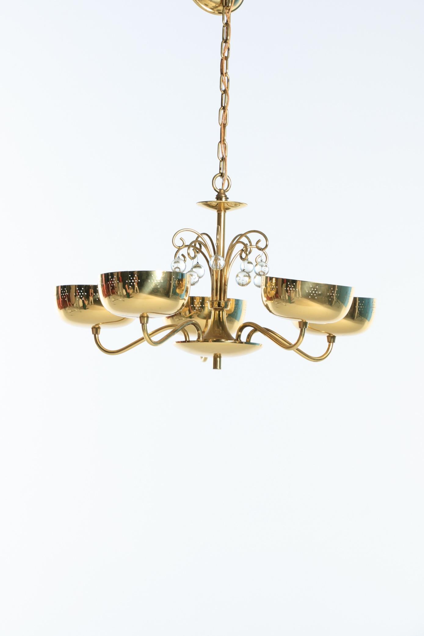 A brass and crystal chandelier attributed to Lightolier, in the style of Paavo Tynell. Possibly designed by Gerald Thurston. Perforated brass upwards lights with crystal balls hanging from top. An elegant design with some whimsy. Want to see more