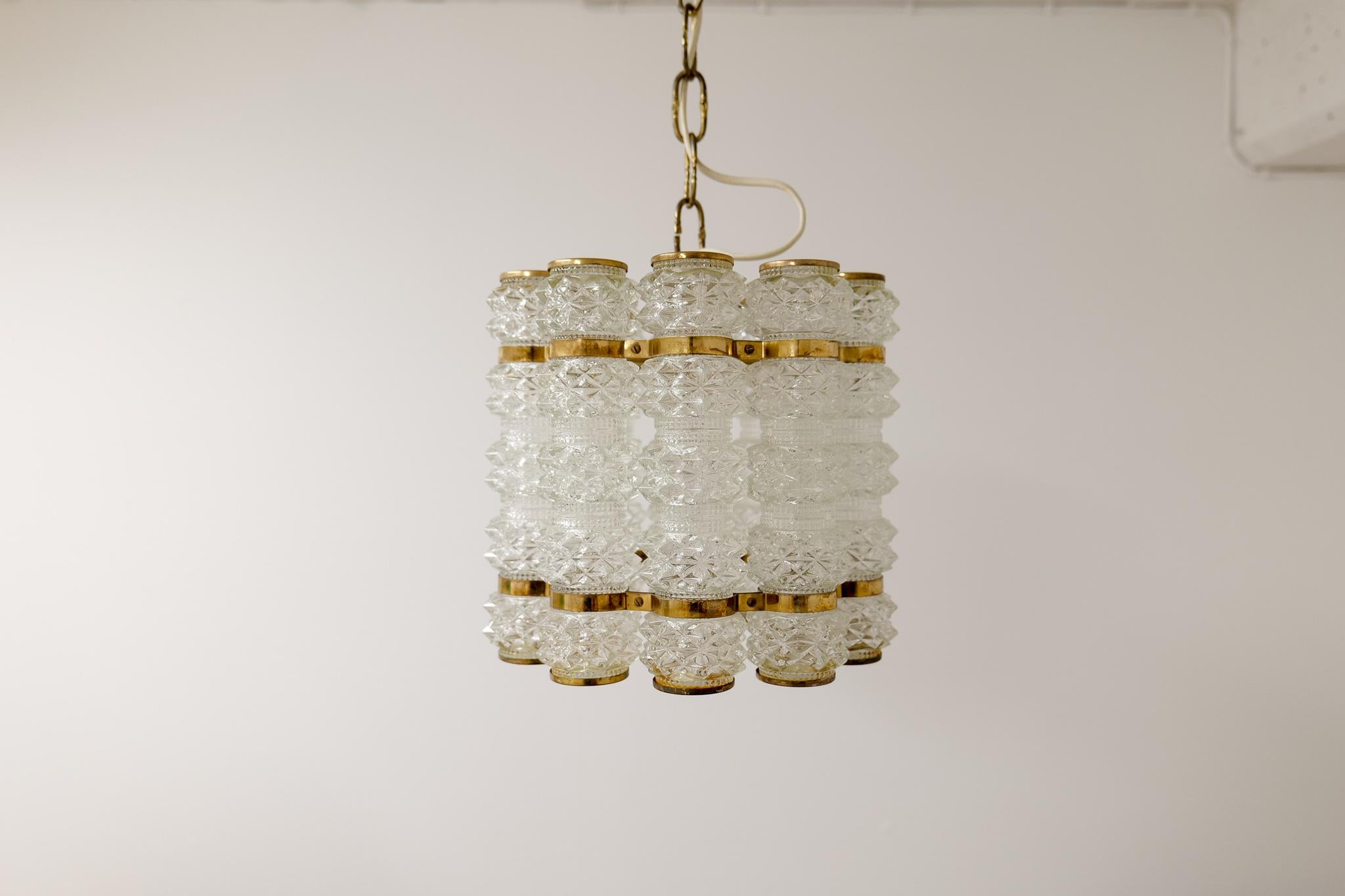 Well-made chandelier with ten-cylinder shaped cupolas in crystallized glass and brass fittings.
Designed by Orrefors and manufactured by Tyringe, circa 1960 second half.

Vintage condition, the brass parts have not been polished.
 