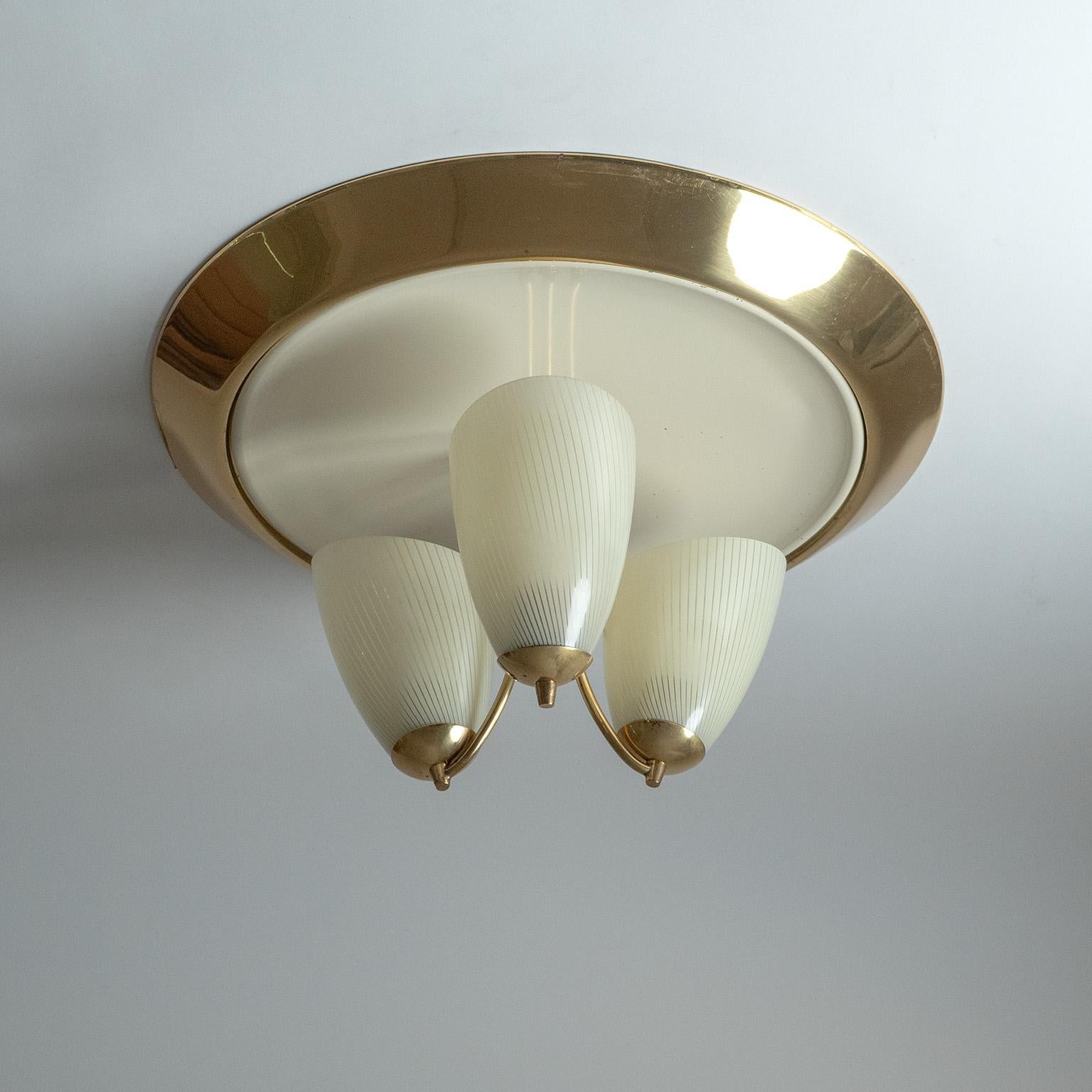 Importante boîte d'encastrement allemande en laiton et verre émaillé, datant des années 1950. Trois abat-jours en verre avec des bandes émaillées sont suspendus à une plaque de plafond laquée avec un large bord en laiton poli. Très bon état