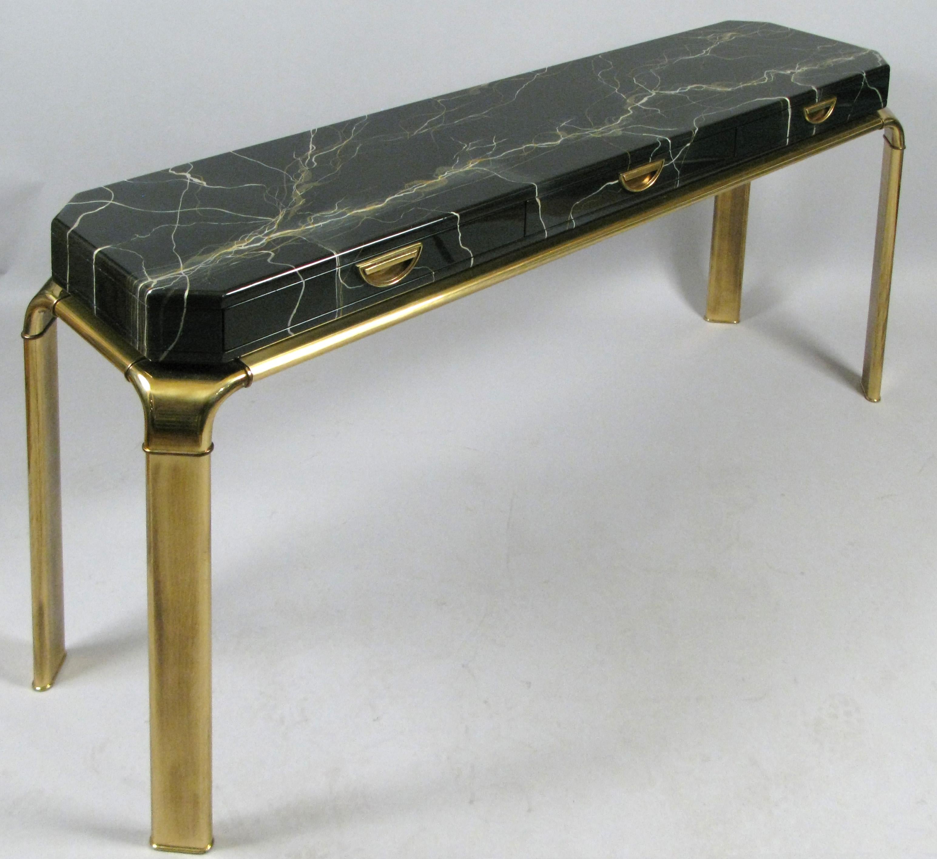 A stunning vintage 1960s console table with three drawers with a brass base by Widdicomb. the case is expertly finished with a faux marble finish making it very convincingly appear as a slab of beautifully grained black marble. the three drawers