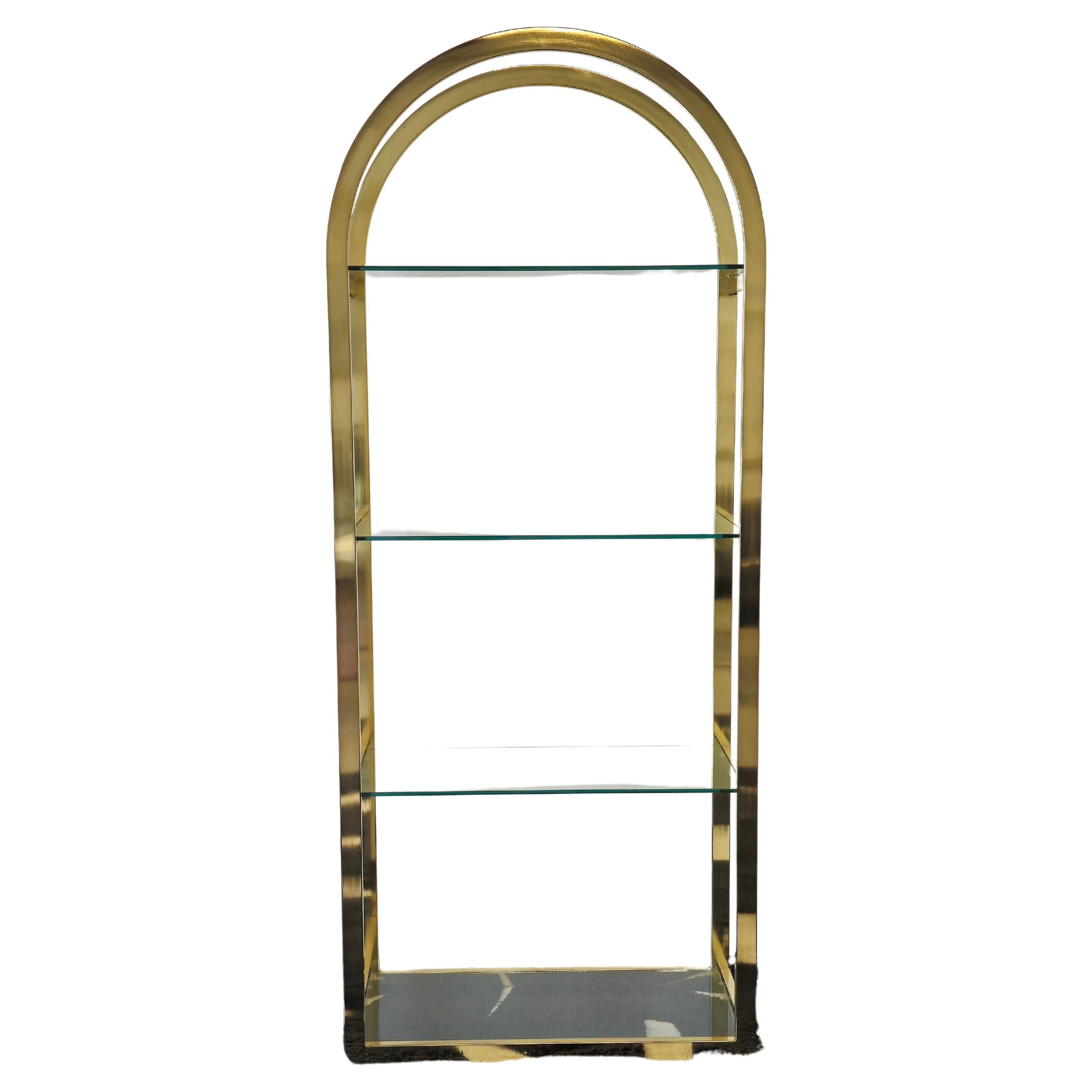 Stunning brass and glass etagere. This etagere has a brass frame with an arch top and floating glass shelves. The brass body is well crafted with seamless lines. There are four glass shelves, three of which sit on the edges of the brass frame giving