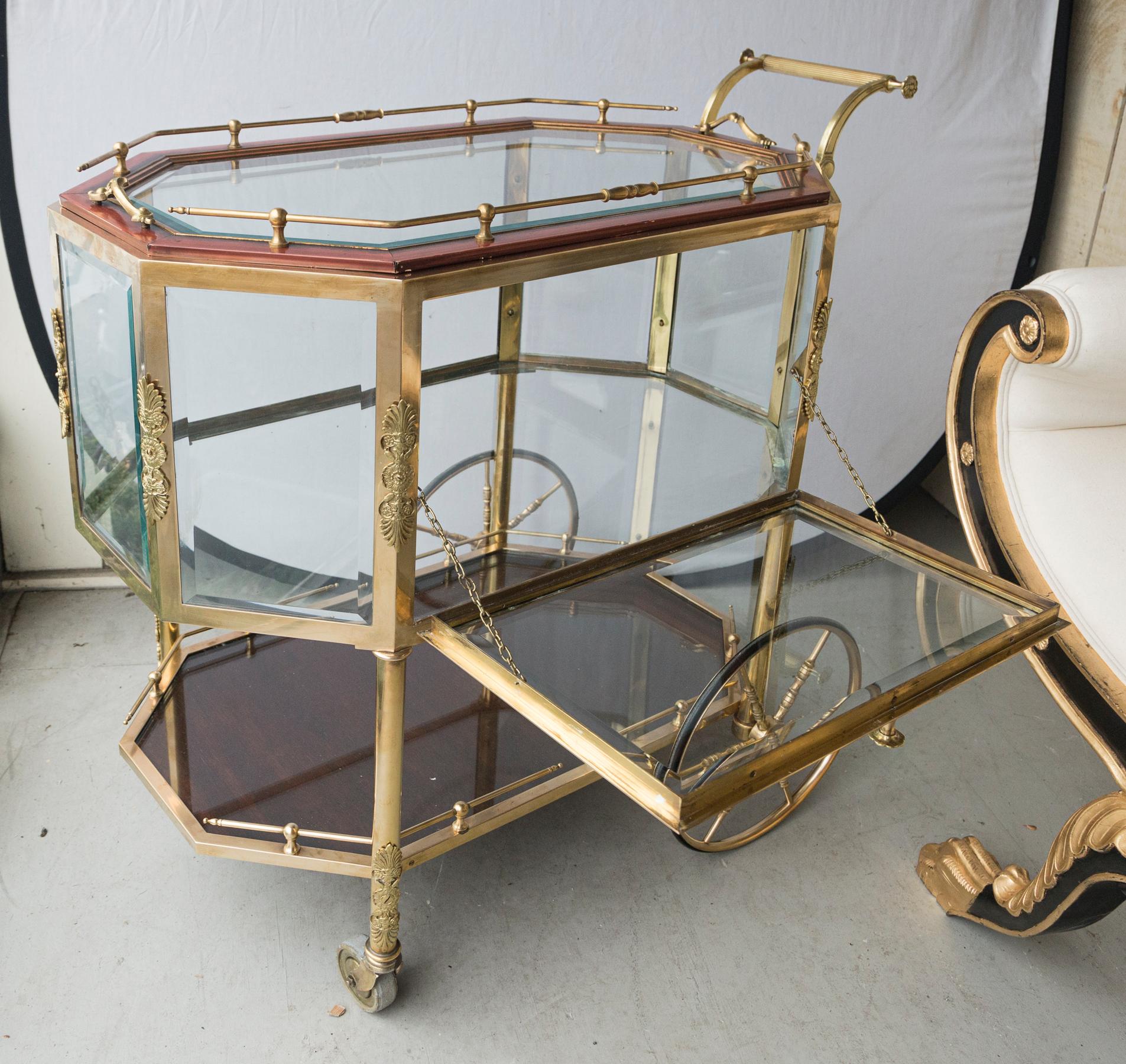 The top of the cart is a lift off glass and painted wood frame tray. There are brass handles at either end and a brass low gallery or fence, on all sides,
The middle section is a drop front door cabinet. The door is attached with chains. It snaps