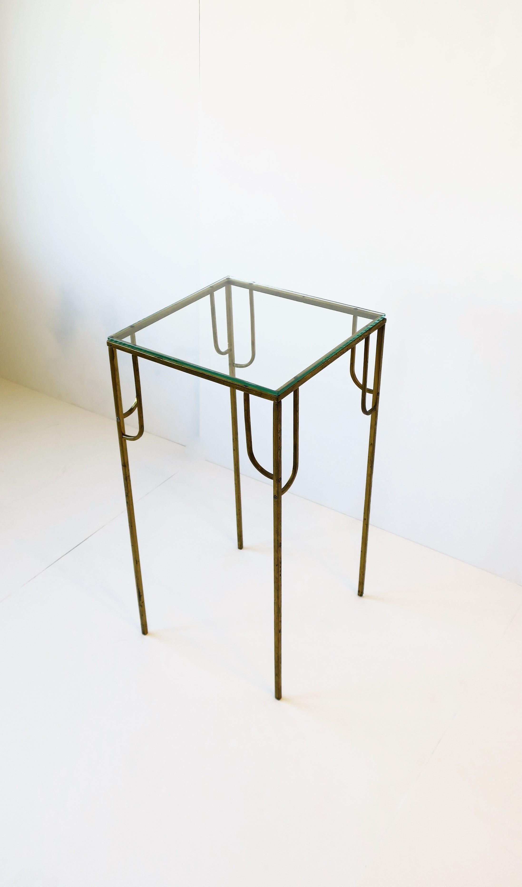 A brass and glass pedestal table in the Art Deco Modern style, circa 1970s. Pedestal frame is sold brass with slender legs and modern deco design details. A great piece for sculpture, display purposes, plantstand, tall end table, etc.

Dimensions: