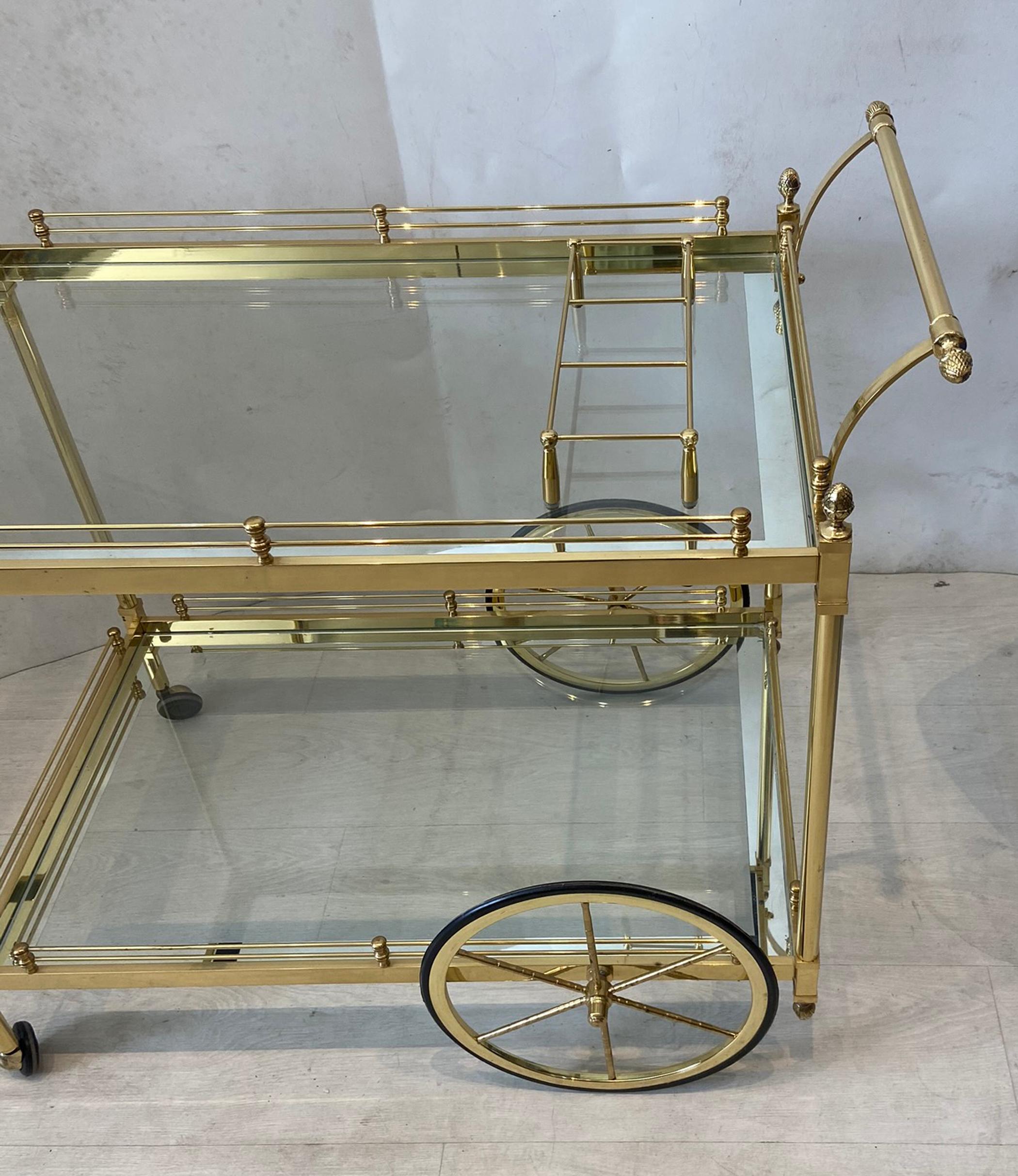 Vintage brass bar or tea cart. Polished and lacquered brass finish is in very good condition. Large spoke wheels in back for easy mobility. Glass shelves on both upper and lower level all in very good condition.