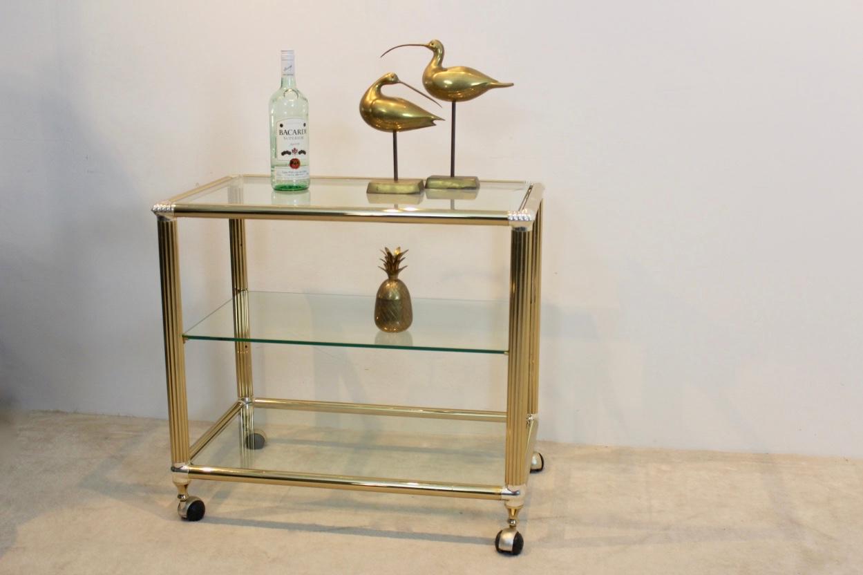 Stunning Belgian bar cart in brass and glass with tempered transparent glass. The heavy metal frame has a total original brass finish with silver plated edges with some patina. The table features three tiers, the middle one is flexible. The cart is