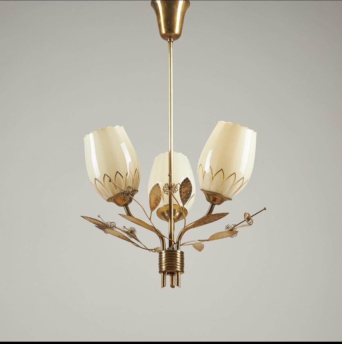 This sophisticated 1950s chandelier, attributed to Finnish design master Paavo Tynell for Itsu, features hand-worked brass and lustrous lattimo opaline glass with refined gilded accents. Measuring approximately 42 cm in diameter and 68 cm in height
