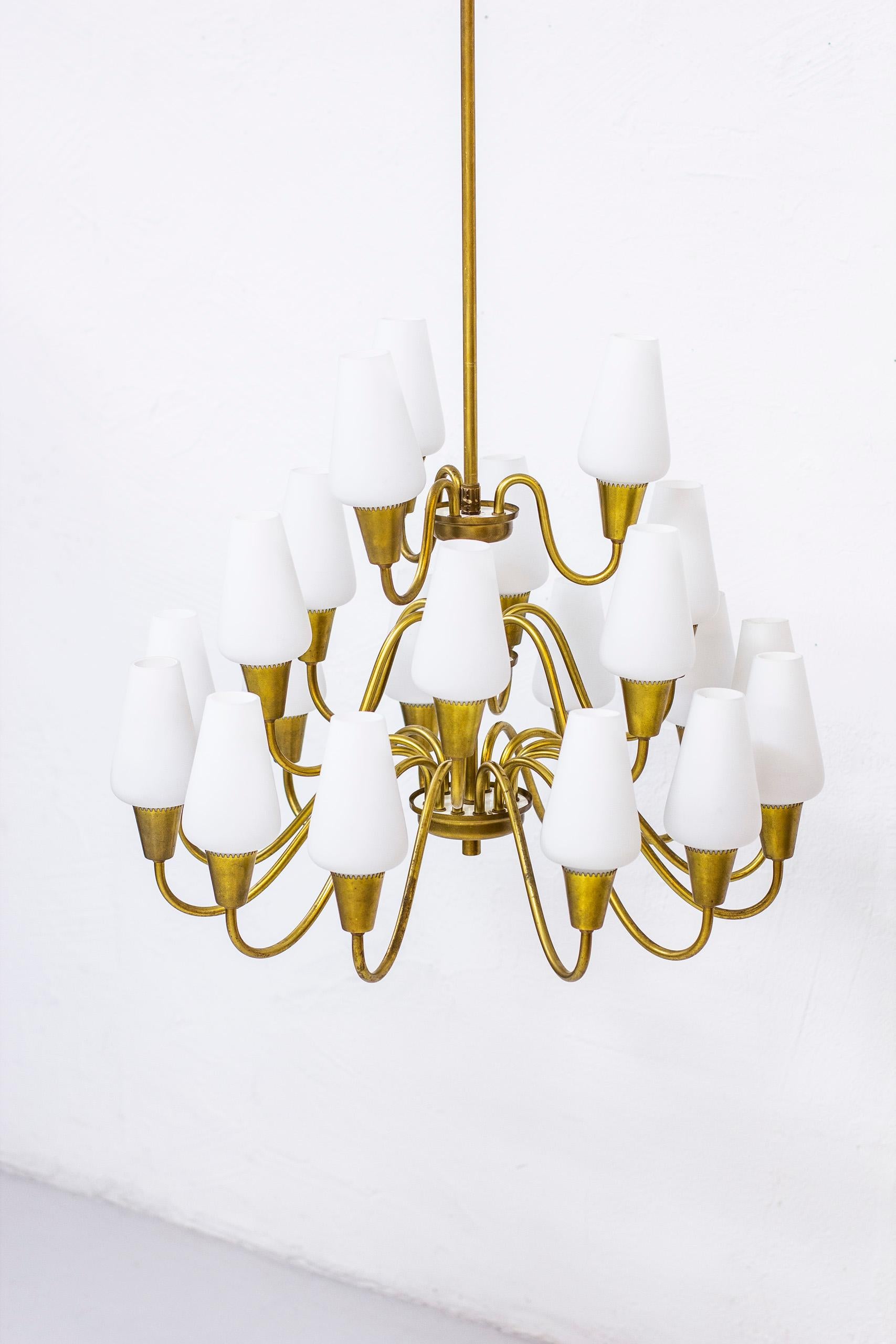 Chandelier produced in Norway by Arnold Wiigs Fabrikker. Made from solid brass with opaline glass shades. Twenty one arms on three levels. All lamps working. Very good vintage condition with all original glass shades intact. 

Height of the lamp