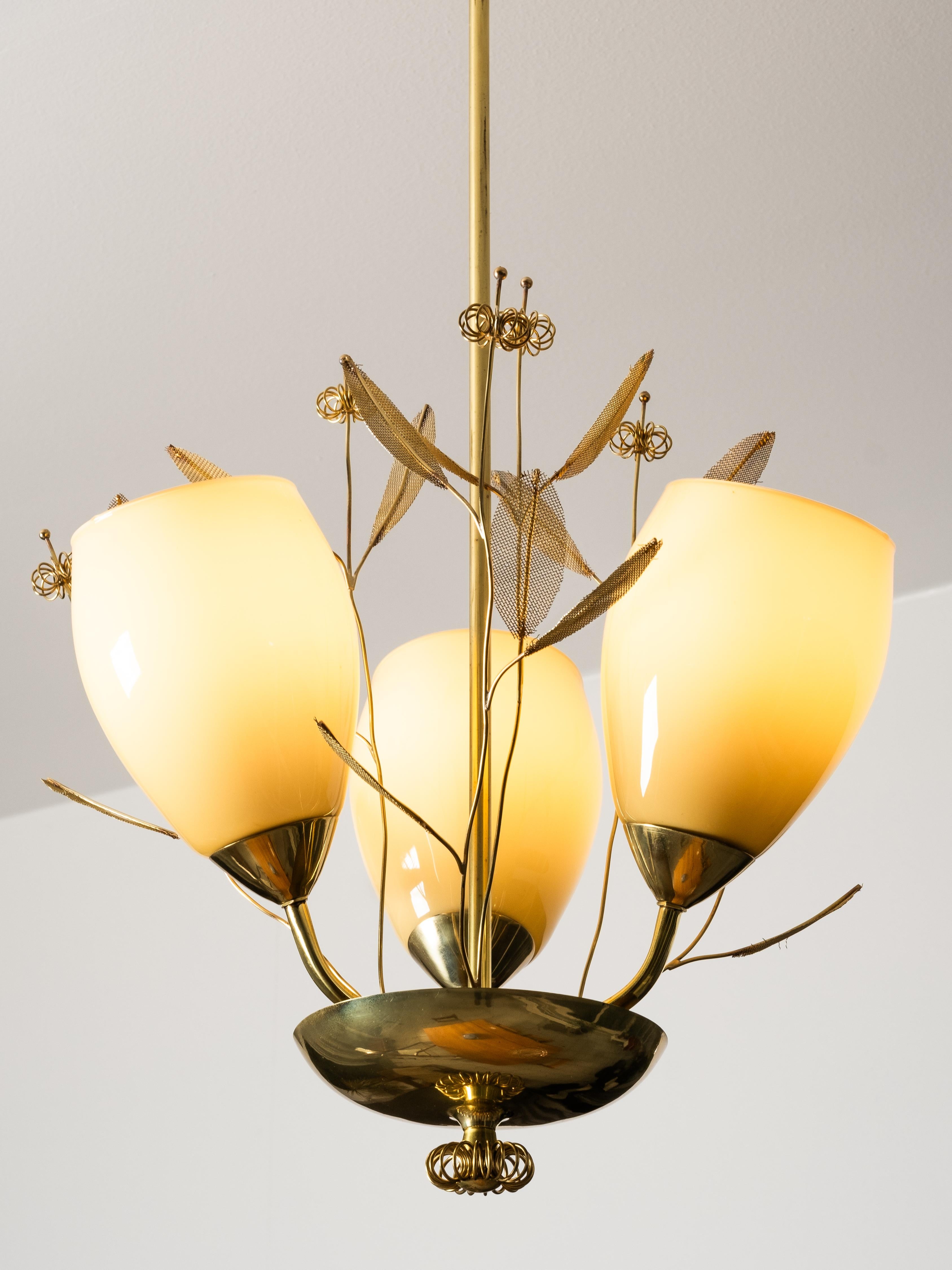Una lámpara de araña finlandesa de mediados de siglo de Sievä, fabricada en la década de 1950. La araña está fabricada en latón pulido con detalles de inspiración floral y elementos de latón en forma de hoja, combinados con pantallas de cristal