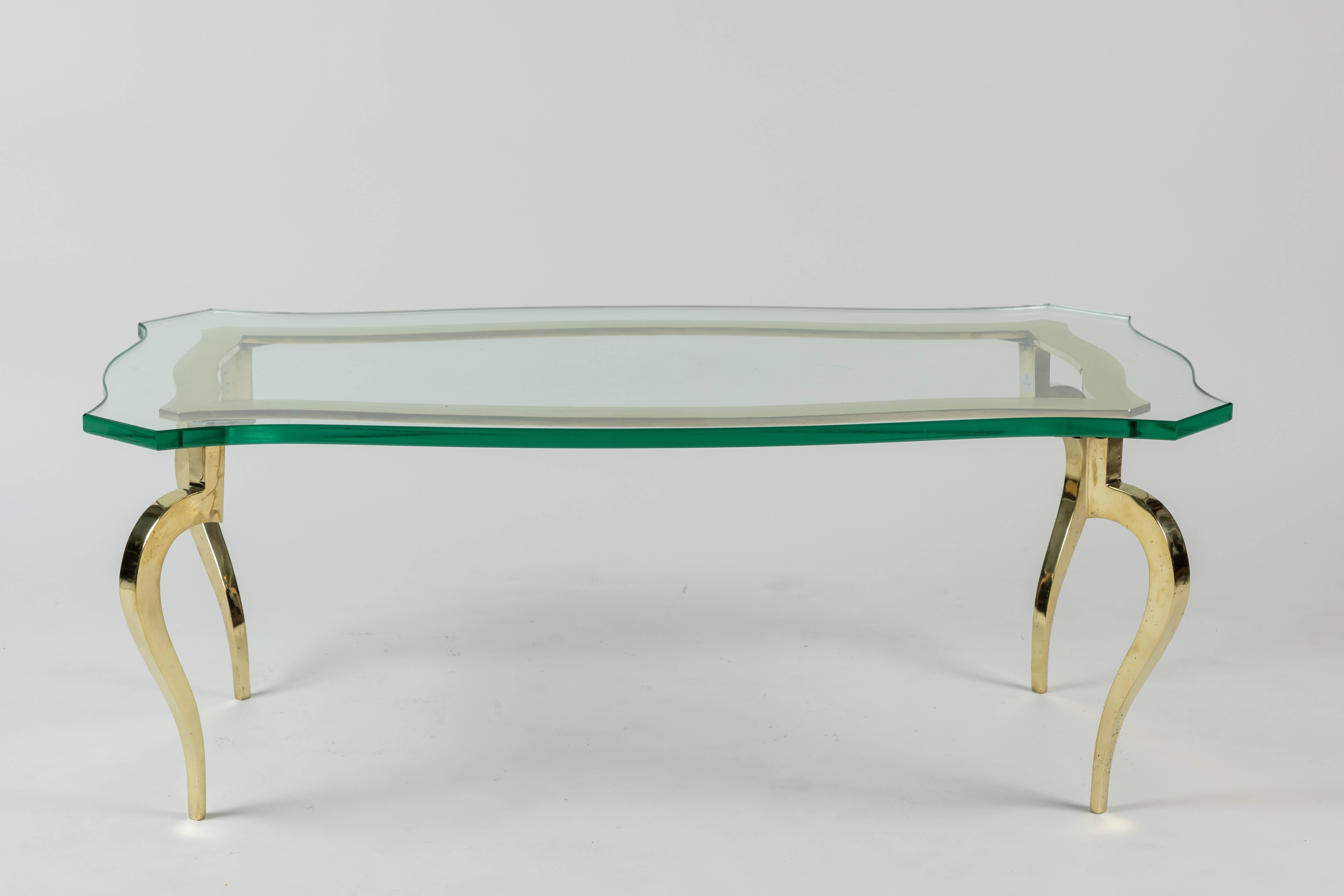 Slick glass-top cocktail table with brass French legs. The glass top mimics the shape and the curves of the brass skeleton base below.