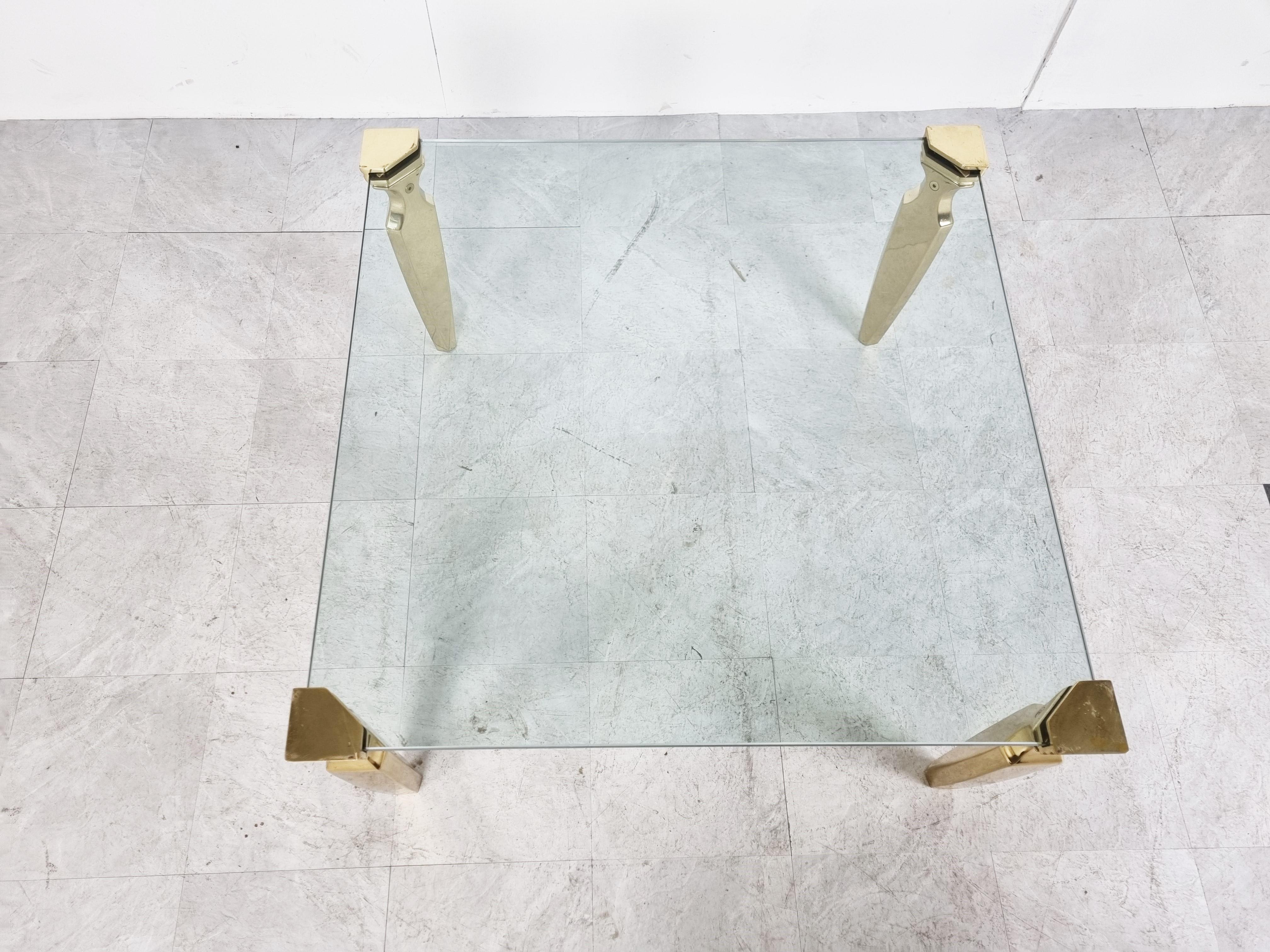 Square clear glass coffee table with elegant brass column legs.

The table has the same design features as Peter Ghyczy's coffee tables. the glass is clamped in the corners of the legs.

Designer is unknown but what we do know is that its a