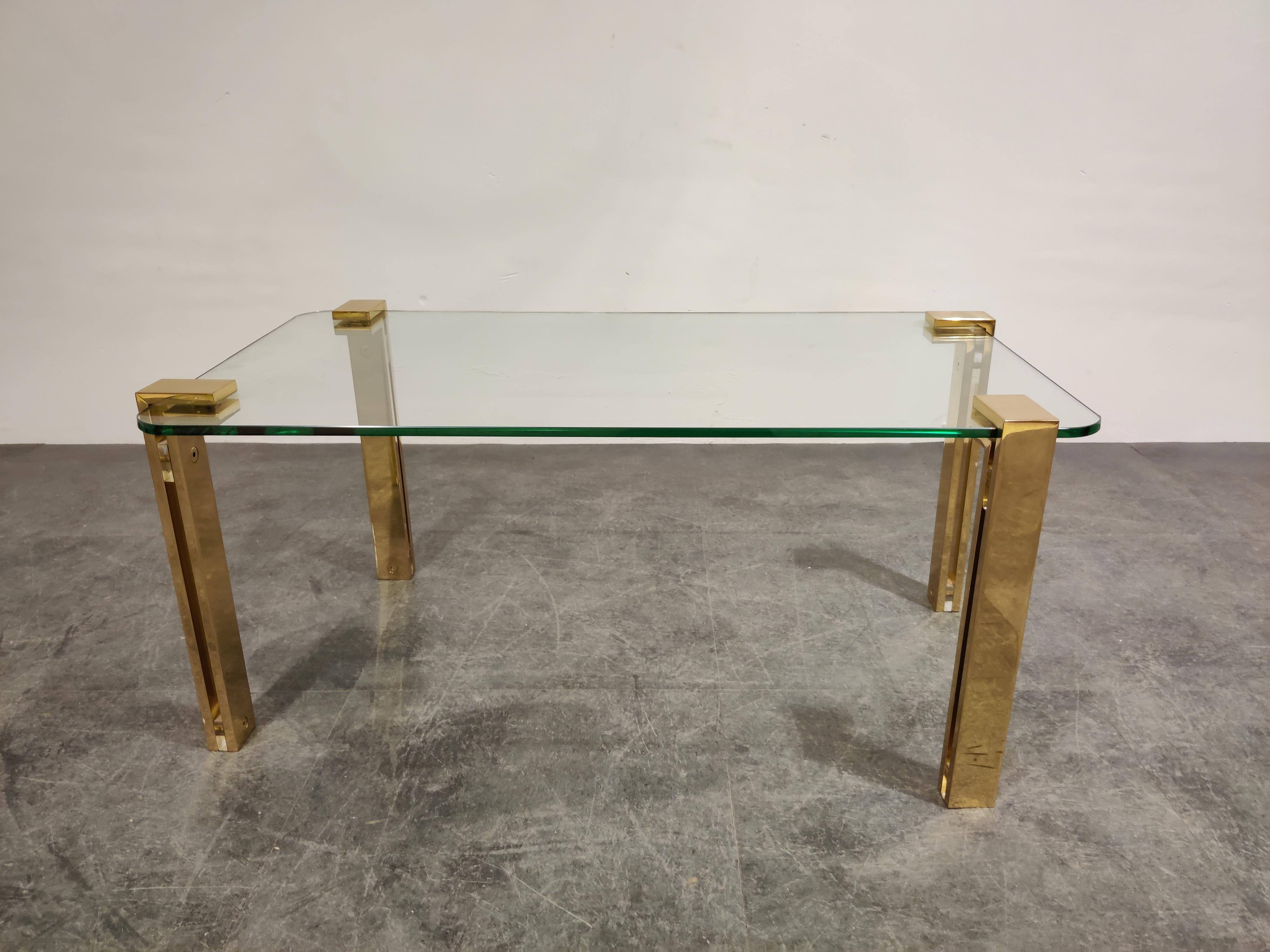 Rectangular clear glass coffee table with brass legs.

The table has the same design features as Peter Ghyczy's coffee tables with a unique way to support the glass so it appears to be floating.

The designer has used heavy two-part brass legs