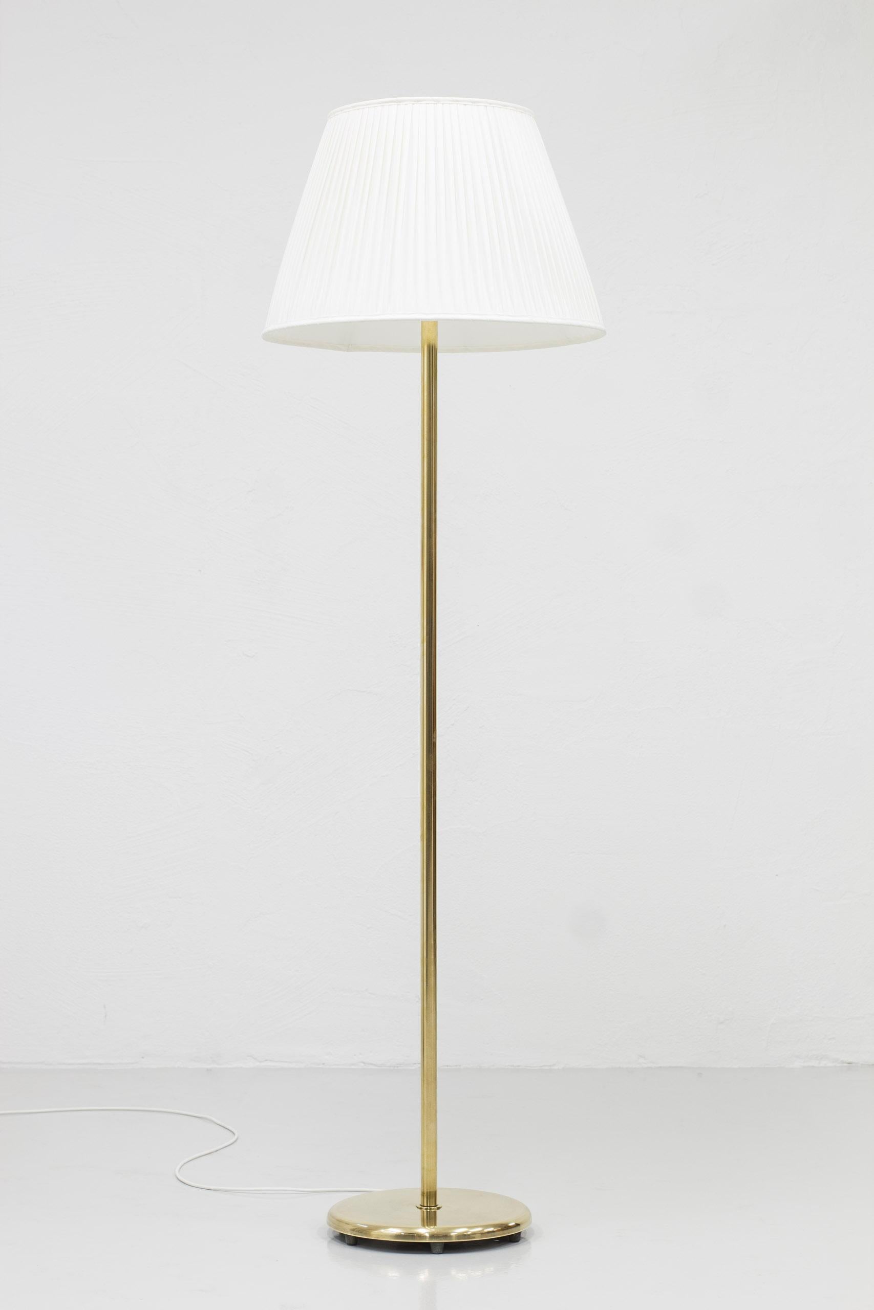 Floor lamp model 15193 designed by Harald Notini. Produced by Böhlmarks in Sweden, circa 1940s-1950s. Made from solid polished brass with inner glas shade in opal glass. New hand sewn pleated lamp shade in off white chintz fabric. Chord light switch