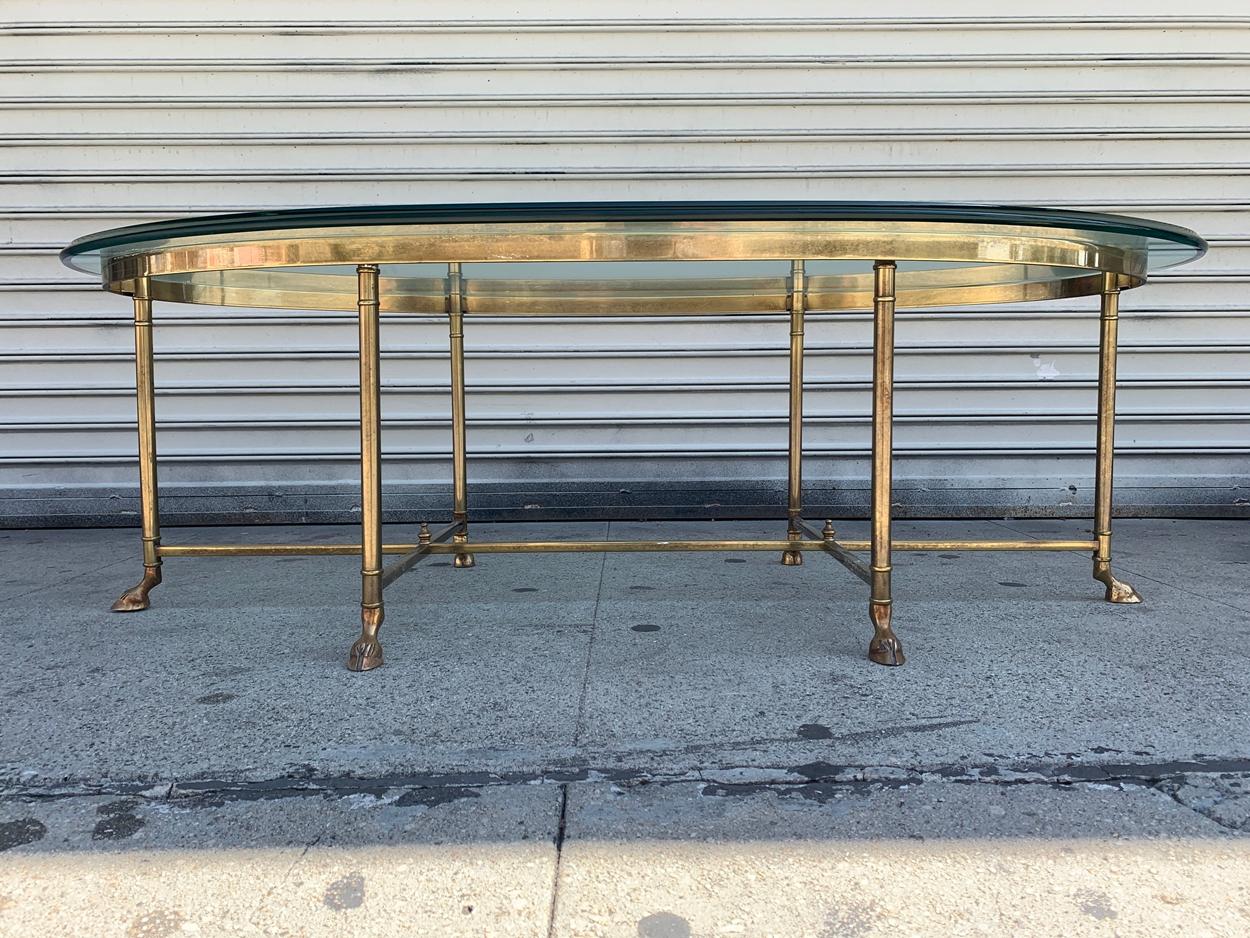 A gorgeous midcentury Hollywood Regency brass and glass coffee or cocktail table by La Barge.

 The table features a stylish base with brass legs and stretchers and unique hooved feet. The oval beveled glass top is in very good condition.

