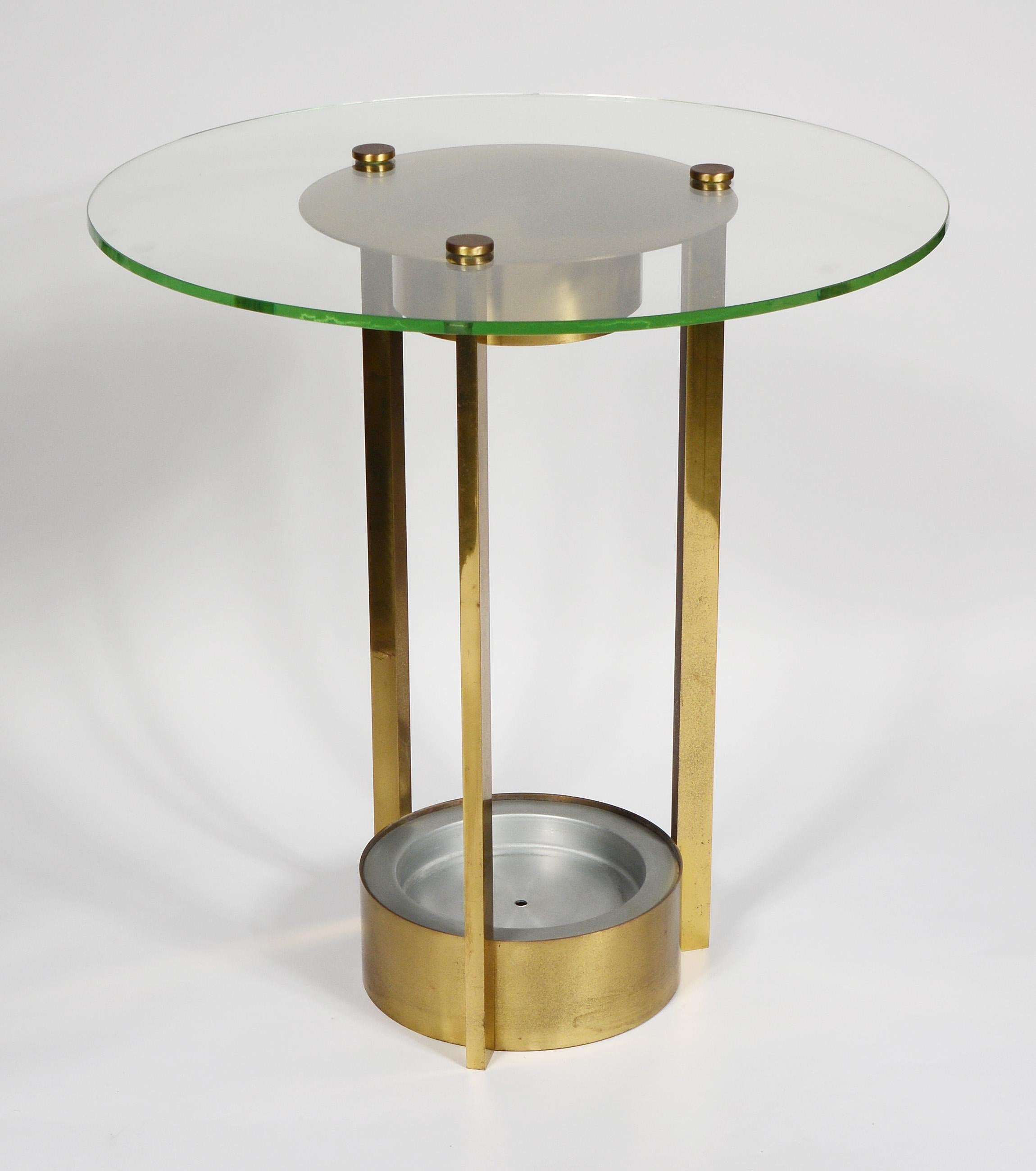 Modernist side table in brass with a glass top. This table has a small bulb in the underside of the top to illuminate any object placed in the base. This had a glass cylinder vase in the originally. The top is the original pale green glass. There is