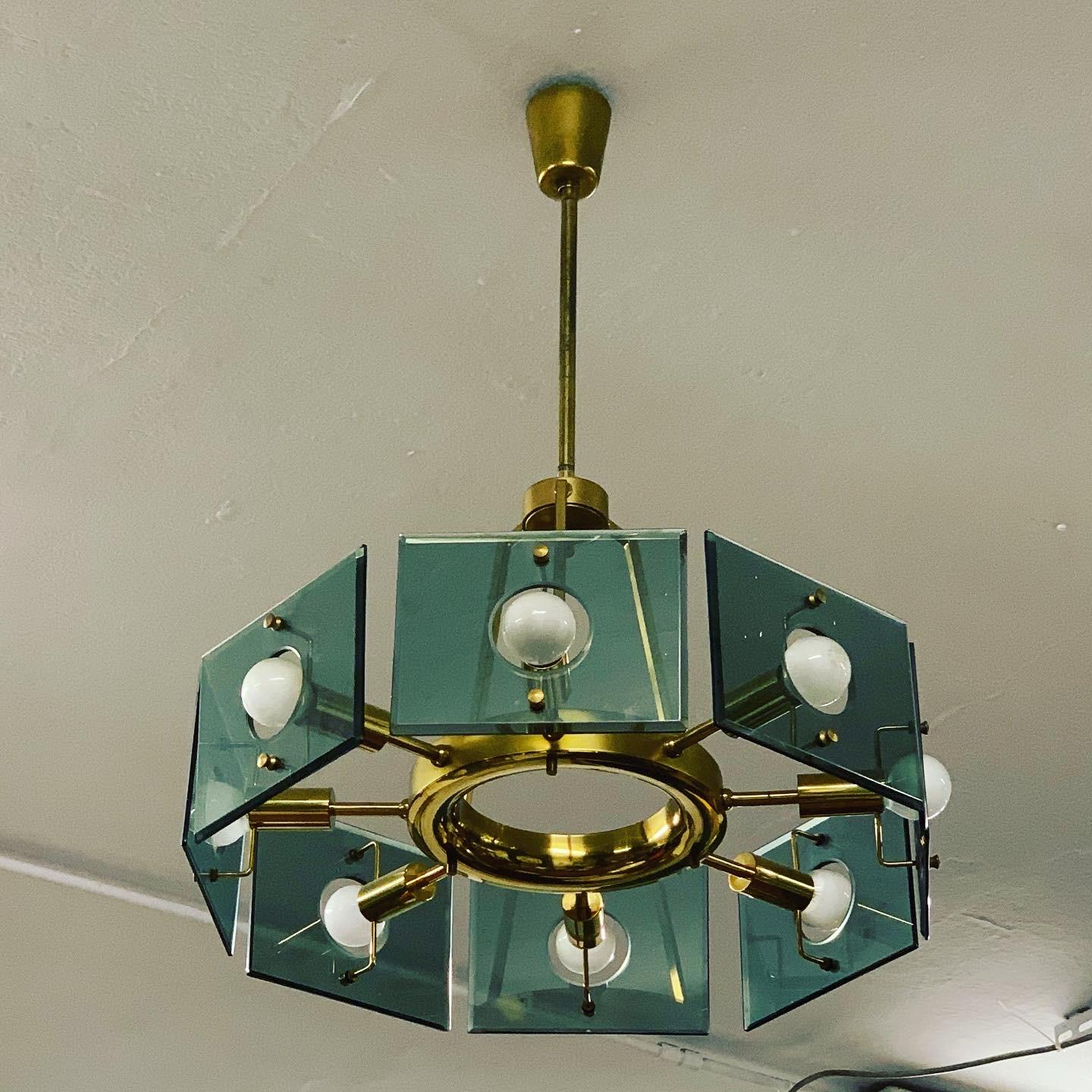 Italian chandelier by designer Gino Paroldo, produced by the company Dino Dei. The luminaire consists of a brass stem, which is developed into a round-shaped halo with 8 light points covered with glass squares that are lightly colored on the outside.