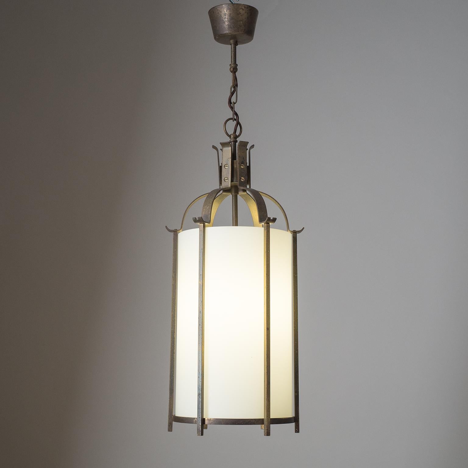 Fine Art Deco brass lantern from the 1930-1940s. Cage-like brass structure with a tubular glass diffuser with white inner casing. Heavy patina on the brass and a few chips on the glass, hidden by the vertical stems. One original brass E27 socket