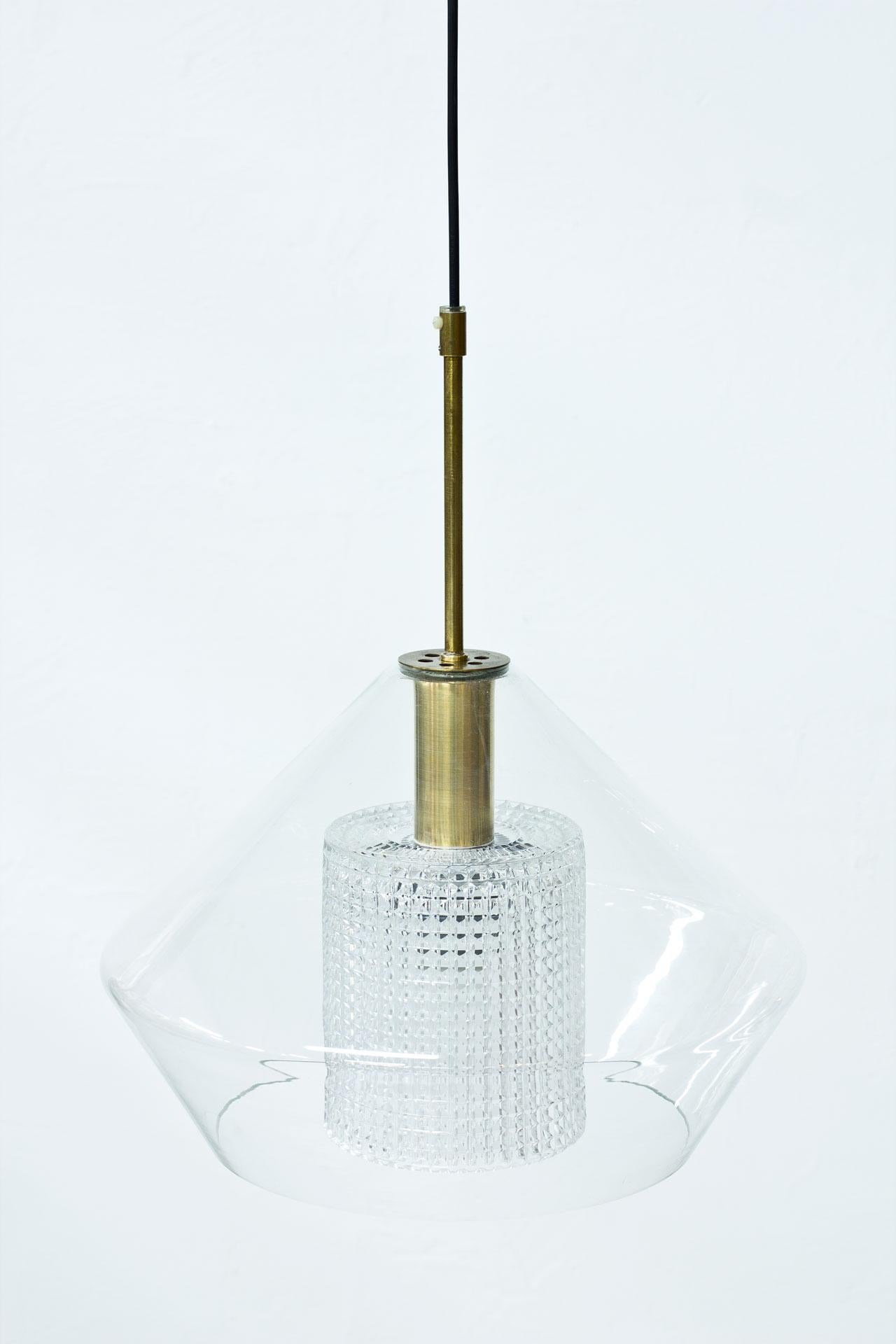 Pendant lamp designed by Carl Fagerlund for Swedish glass company Orrefors during the 1960s. Outer cup in clear glass with a cylindrical diffuser in clear pressed glass. Brass fittings.
New electricity.