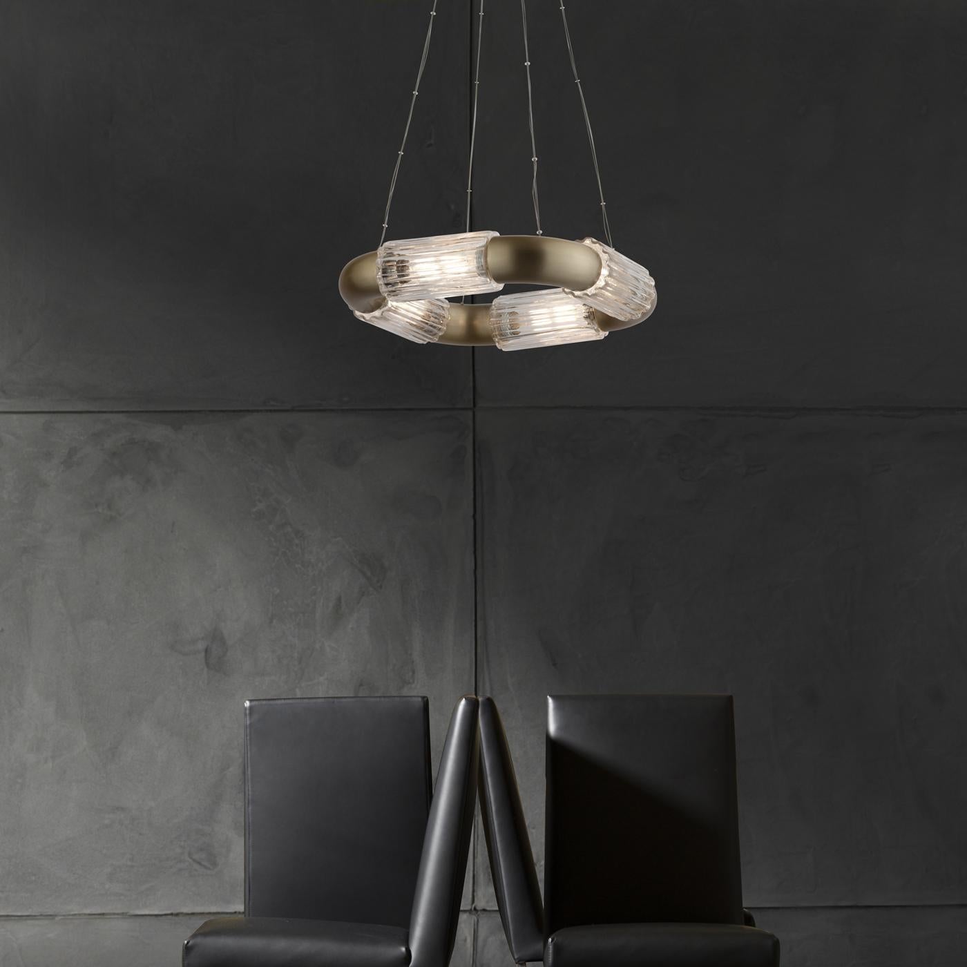 Suspended from thin metal wires, this stunning pendant lamp showcases a horizontal frame alternating cylindrical sections in satin brass with four cylindrical grooved diffusers, each hosting a tubular LED source (E14 and 4W each). Thanks to its