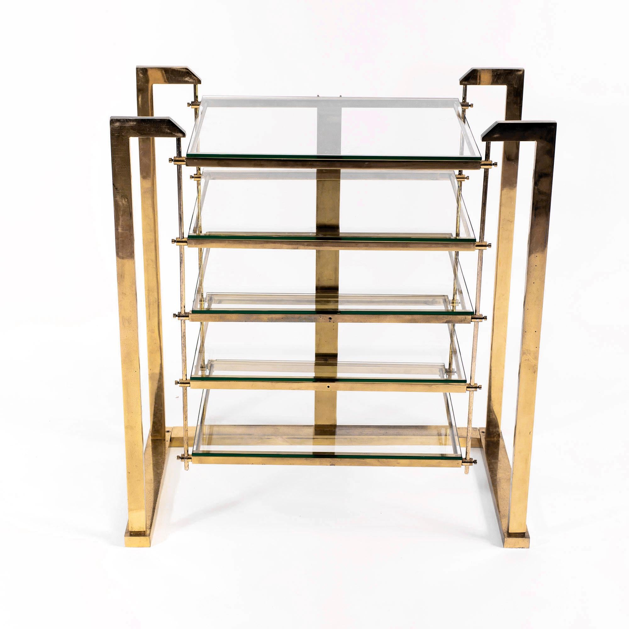 A stylish piece in style of Romeo Rega and Hollywood Regency that can be used as a shelving unit or audio rack. It features an elegant geometric brass structure and five heavy glass shelves.