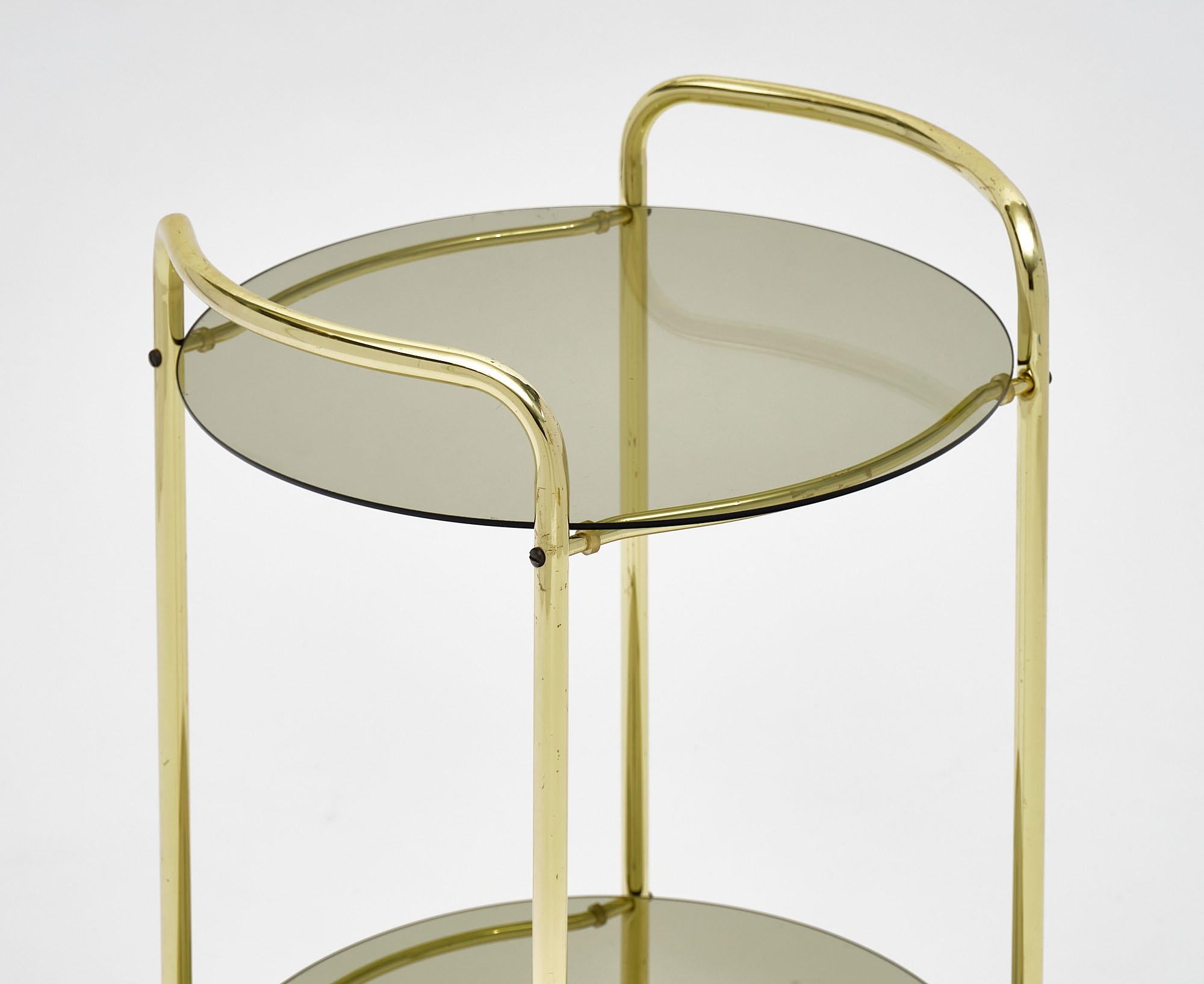 Bar cart from France with original casters. This brass structure features two smoked glass shelves.