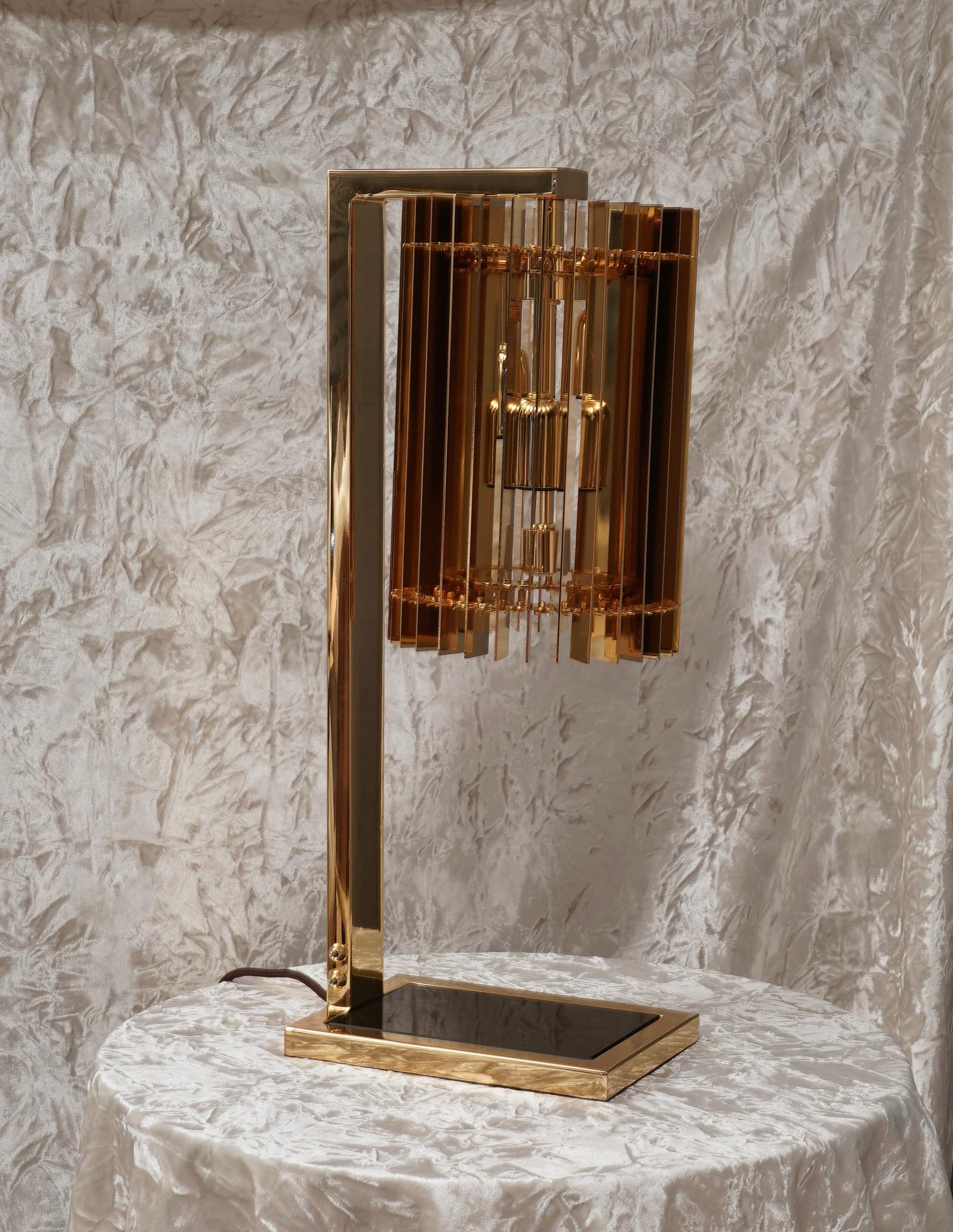 Elegant and stylish table lamp, rich and original design as in the Italian style.

The lamp is composed of a base formed by a brass frame with a black colored glass in the center, from which a brass arm unwinds and connects it to the lampshade; this