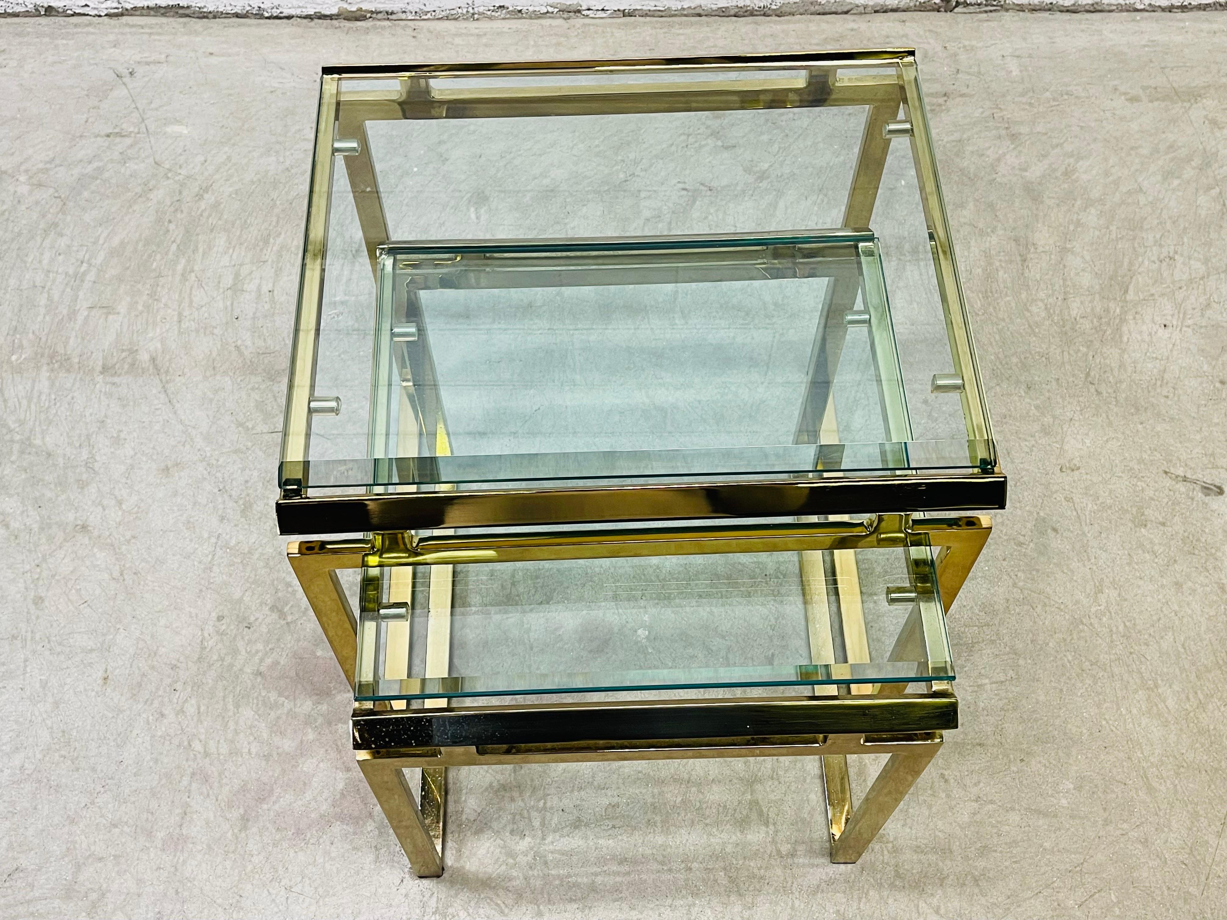 Vintage 1980s pair of brass and glass top nesting tables. The tables are on a thick brass frame with beveled glass tops. The smaller table measures 17” L x 18” D x 17.5” H. Light wear and tarnish from age and use. No chips to the glass. No marks.