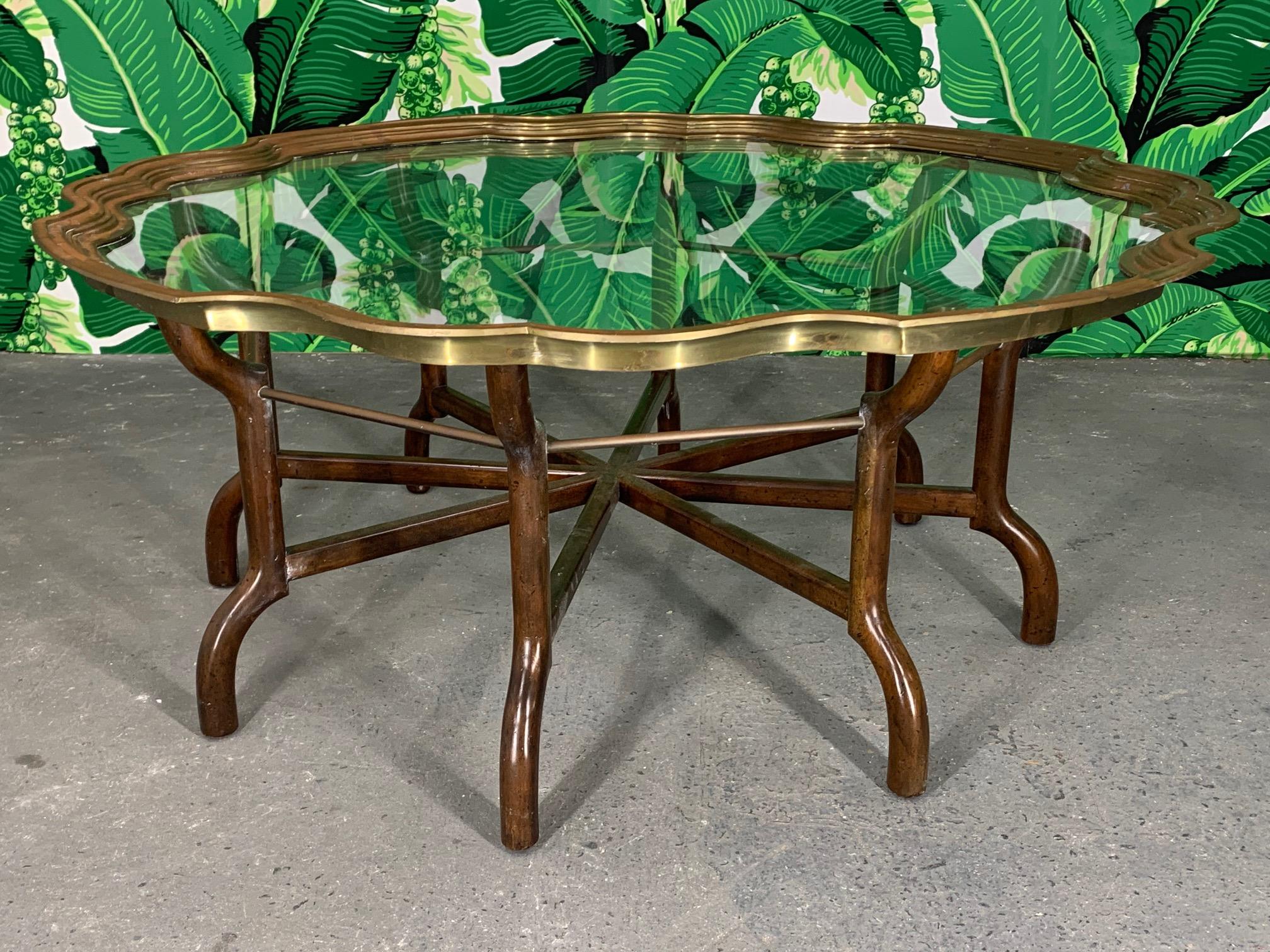 Vintage Baker coffee table features a glass tray top with solid brass scalloped rim. Base is wood with brass stretchers. Good vintage condition with some tarnish to brass.