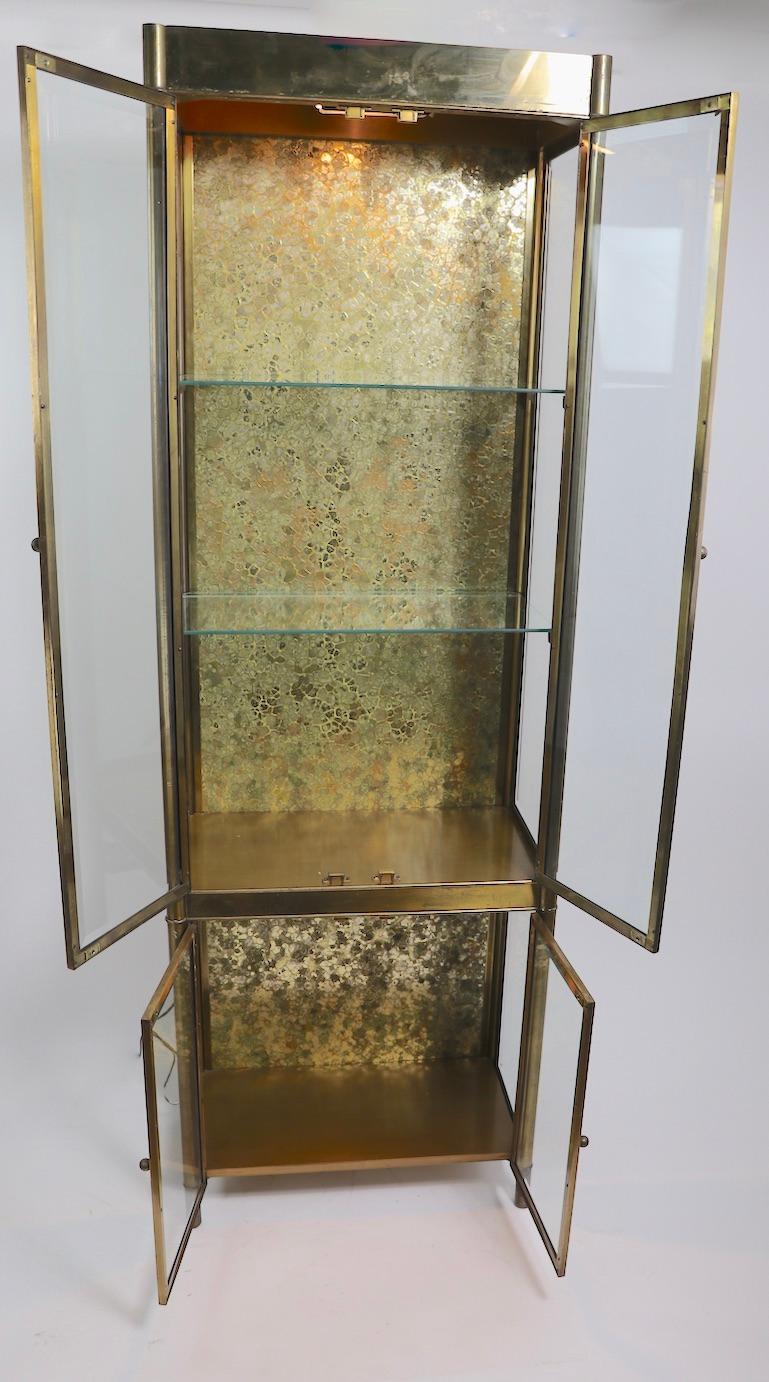Incredible brass and glass display cabinet, vitrine by Mastercraft. This stunning piece features a large upper section over a smaller lower section, each having two doors. The case is of brass, while the glass panels are all bevelled, the upper