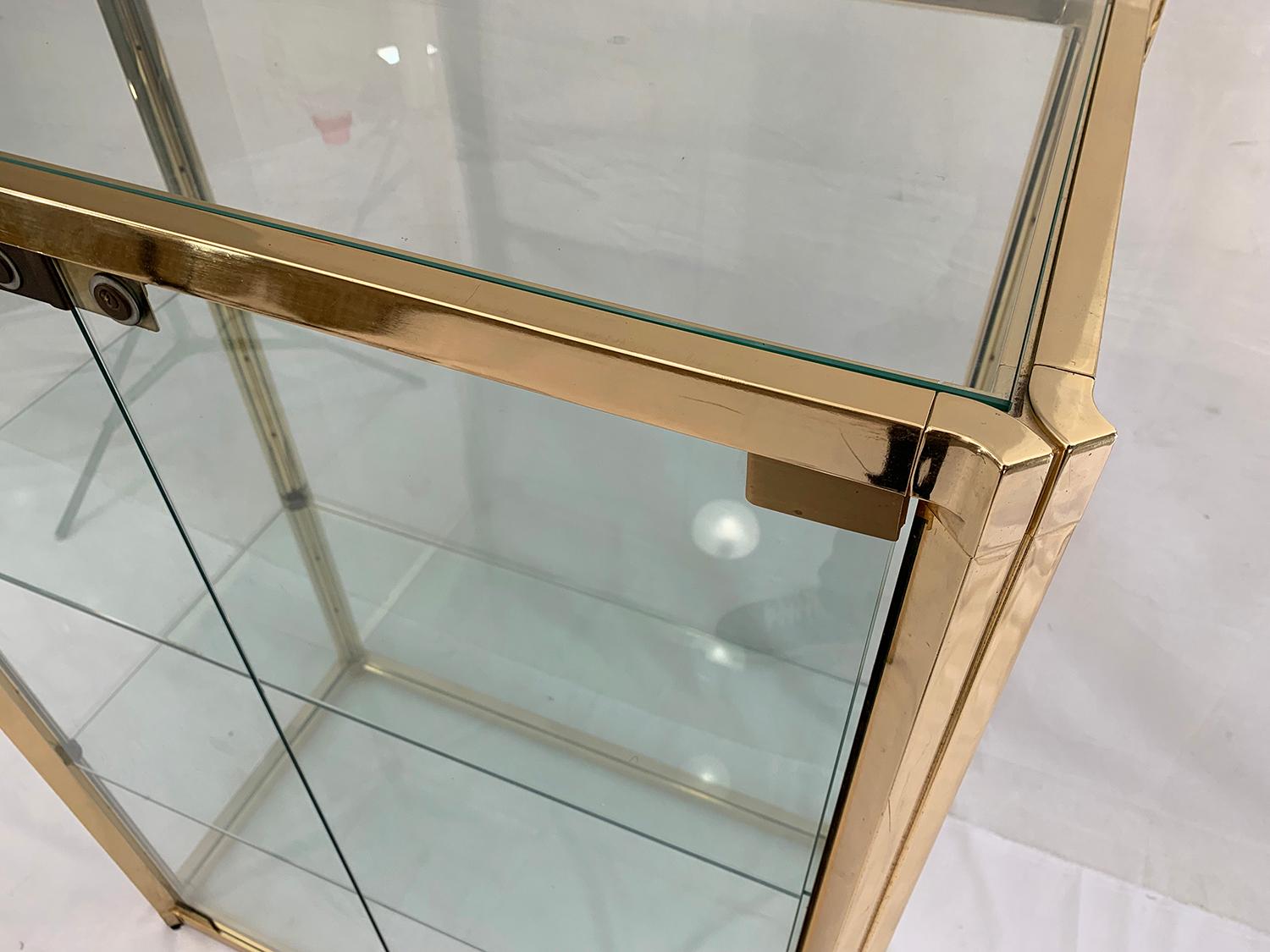 Beautiful vitrine secured by a key lock. The frame is in brass plated aluminium and the shelves including all outer faces and door are made of glass. This showcase is in very good general condition for its age, there are just some minor wear here