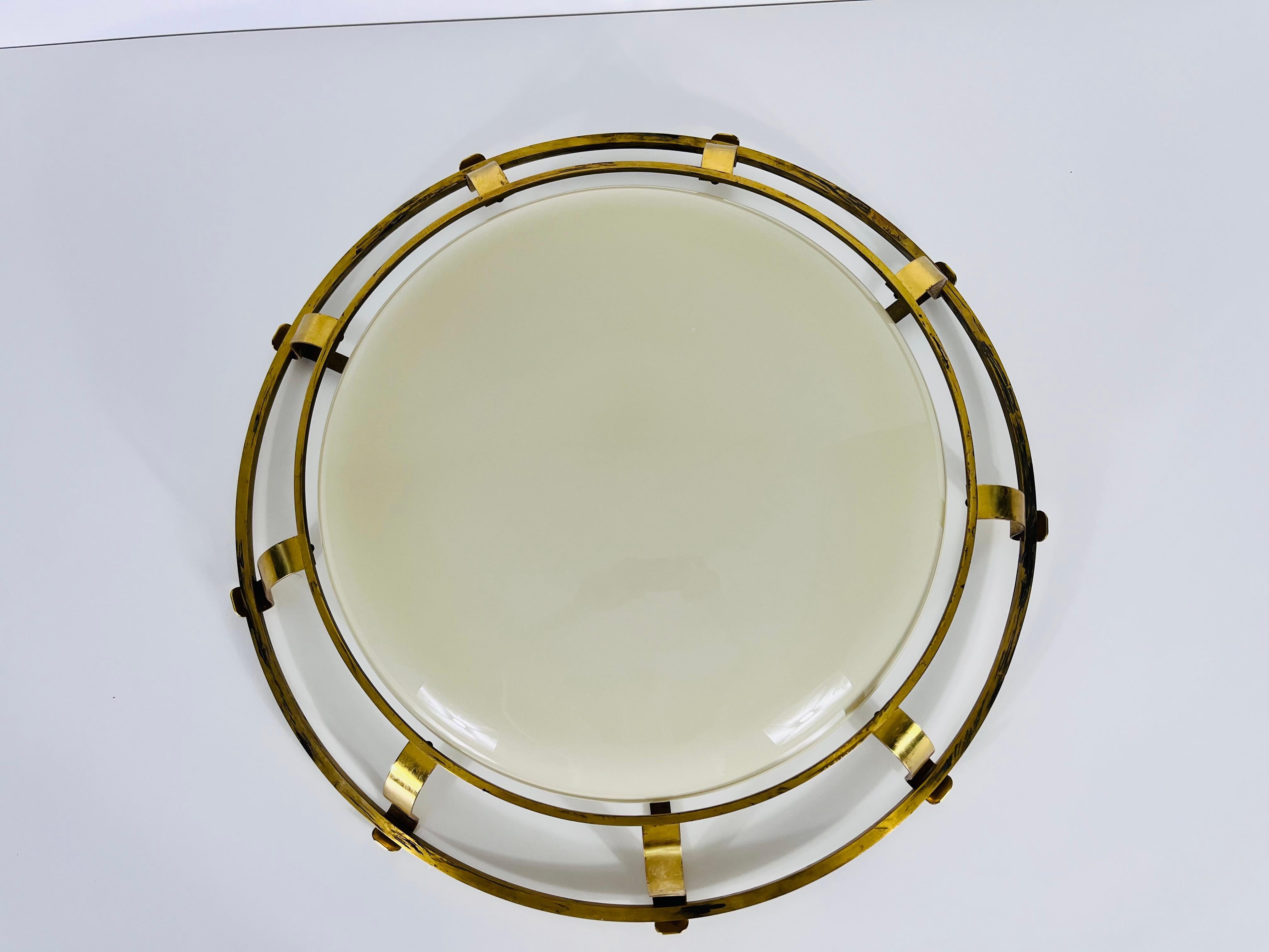 This exquisite Italian ceiling lamp from the 1960s epitomizes the elegance and innovation of mid-century modern design. Featuring a sleek brass frame, the lamp boasts a central glass shade that appears to float effortlessly in the middle, creating a