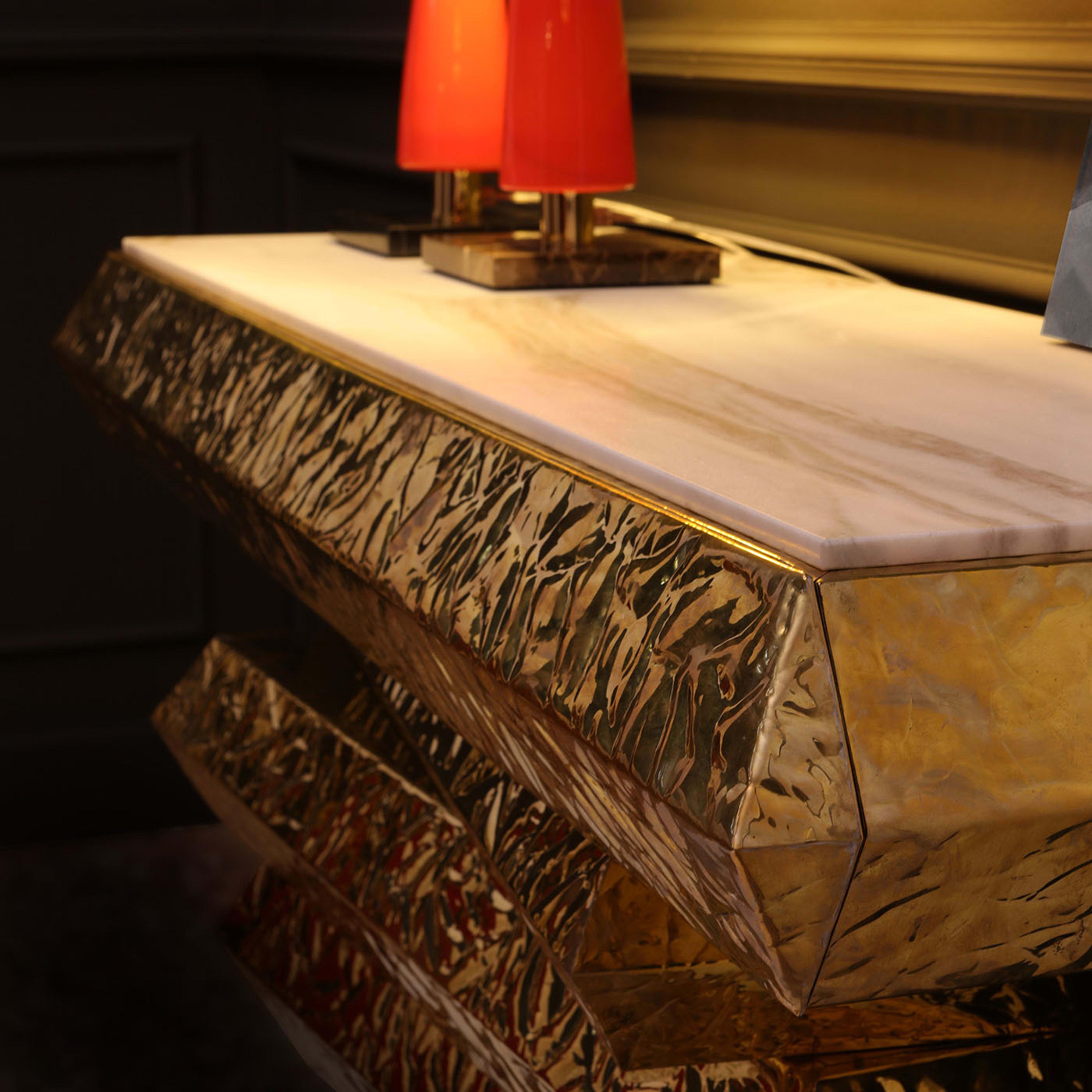 This console was designed to make a stupefying statement in the entryways of exclusive interiors. Achieved thanks to a deft process of manual chiseling, the goldbrick-like elements composing its gleaming structure are arranged in a dynamic way that