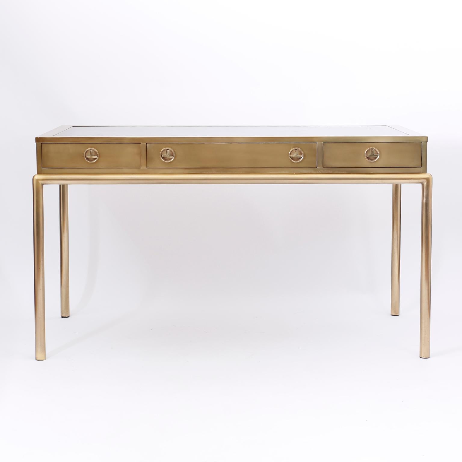 Midcentury three-drawer writing desk with a leather top, stylized Campaign hardware, sleek elegant form, and a chic custom acid washed finish.
  