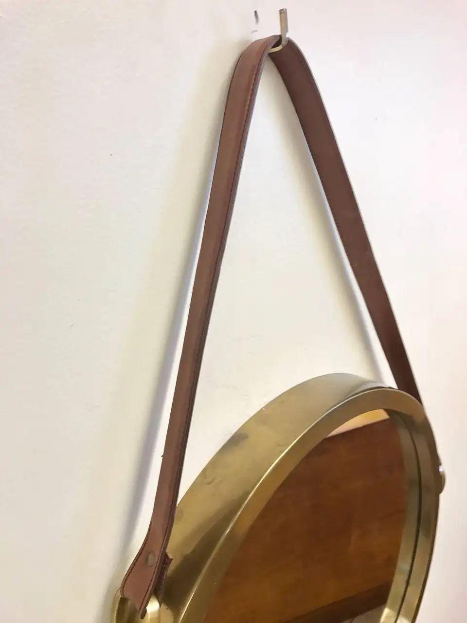 Brass and leather strap mirror style of Jacques Adnet. The bottom half of the mirror is trimmed with brown leather and brass buckles to the side.
Measures: 31.5 height (includes drop of strap) x 21 diameter.