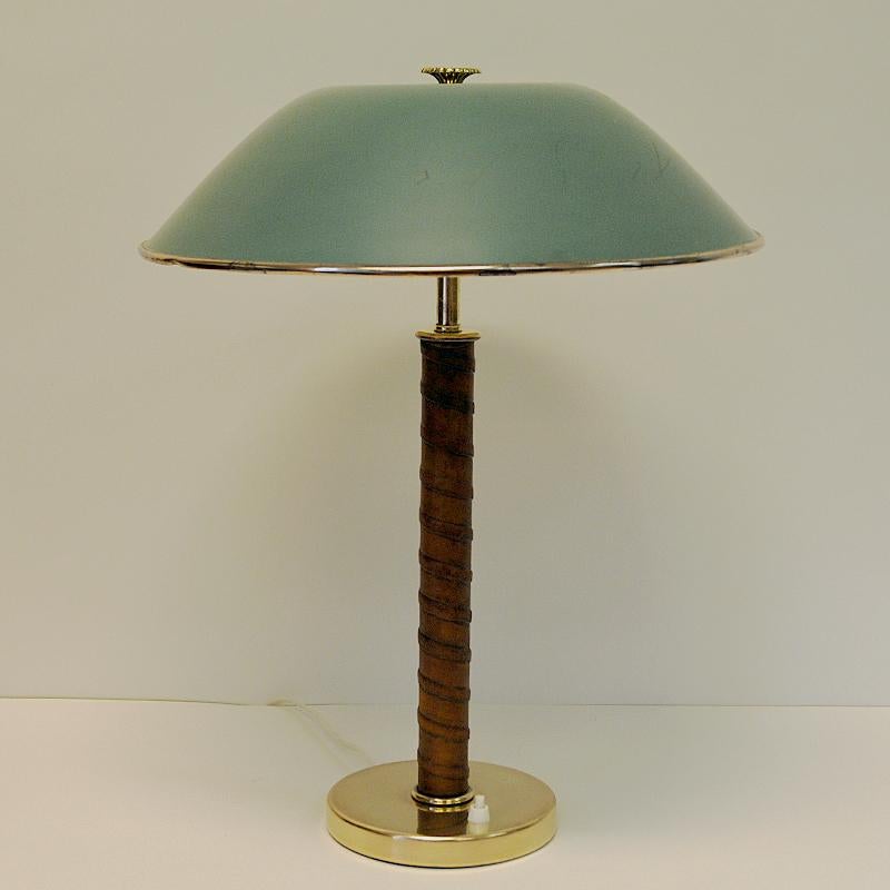 Table lamp from Nordiska Kompaniet (NK) circa 1940s with a round blue/green lacquered brass shade and beaded leather pole. Made in Sweden. Brass foot base which a light button and a decorative flower knob on top of the shade. Two bulbs gives a great