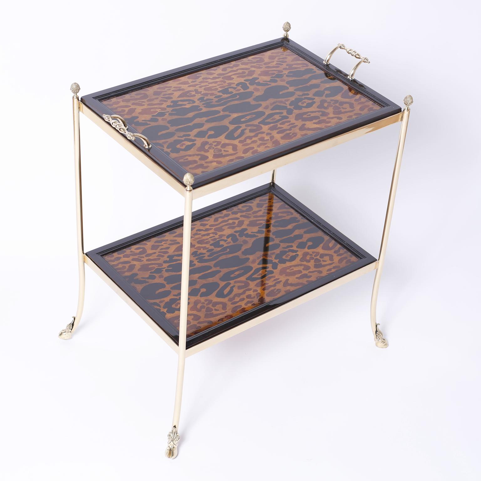 Midcentury two-tiered bar or server with a brass frame having pine apple finials and hoofed feet. The service area has a removable tray that features leopard print under glass on both tiers. Signed Maitland-Smith on the bottom.