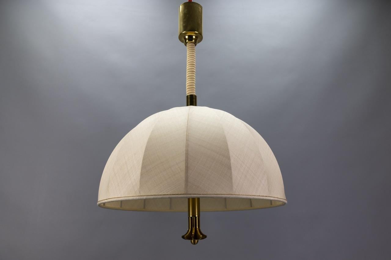 Bellissima lampada a sospensione a tre luci in ottone ad altezza regolabile con paralume in tessuto, Germania, circa 1980.
Realizzata in stile The Modern Scandinavian, questa imponente lampada a sospensione presenta un paralume in tessuto