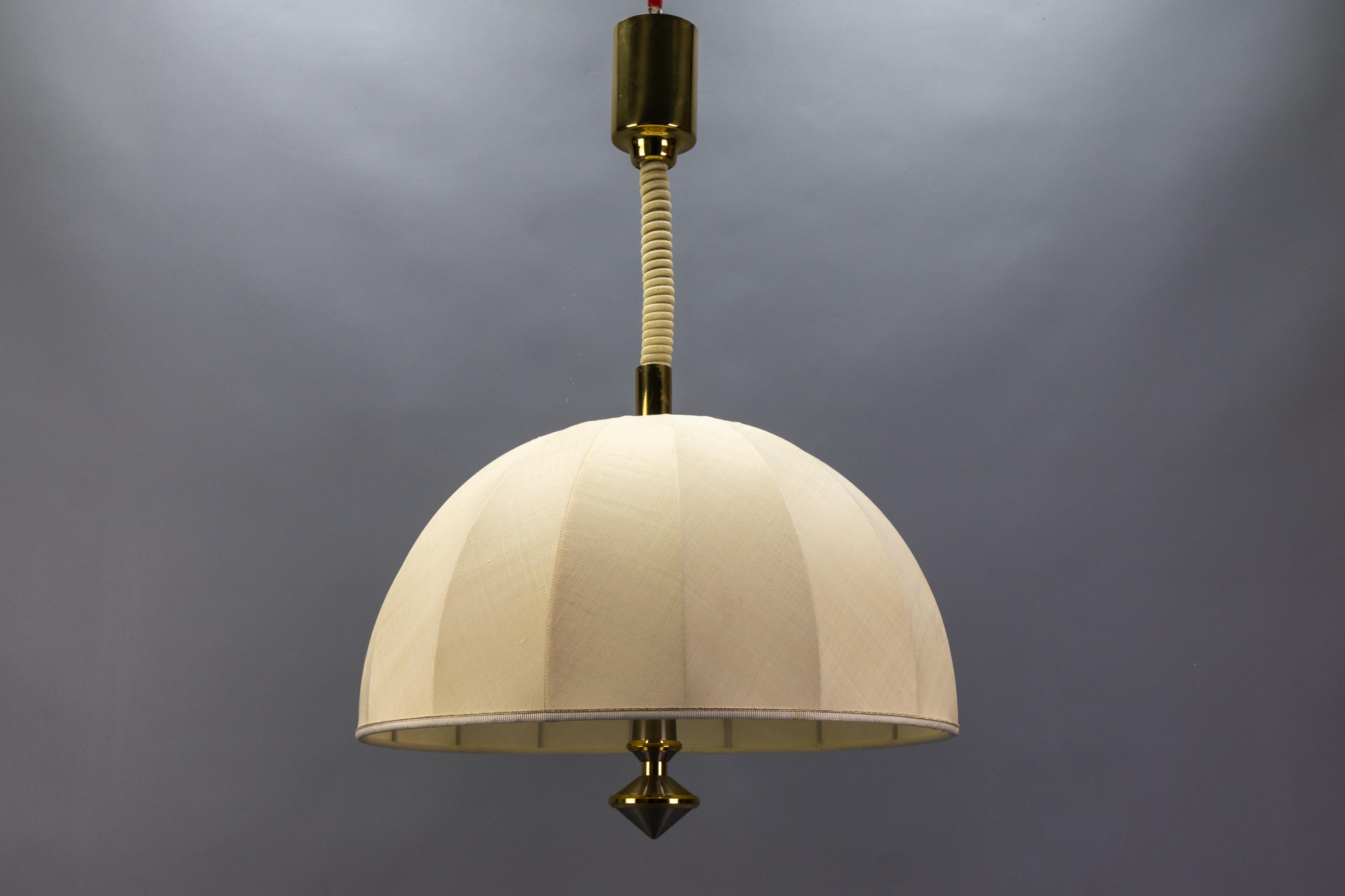 Bellissima lampada a sospensione a tre luci in ottone ad altezza regolabile con paralume in tessuto, Germania, circa 1980.
Realizzata in stile The Modern Scandinavian, questa imponente lampada a sospensione presenta un paralume in tessuto
