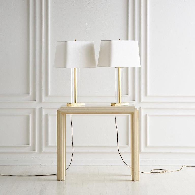 A fabulous pair of French lamps featuring a brass base and center, flanked by two Lucite columns. Each lamp accepts two standard bulbs. Includes new rectangular linen shades. 

Dimensions: 6.75”W x 3.5”D x 27.5”H; shade: 16”W x 10”D x