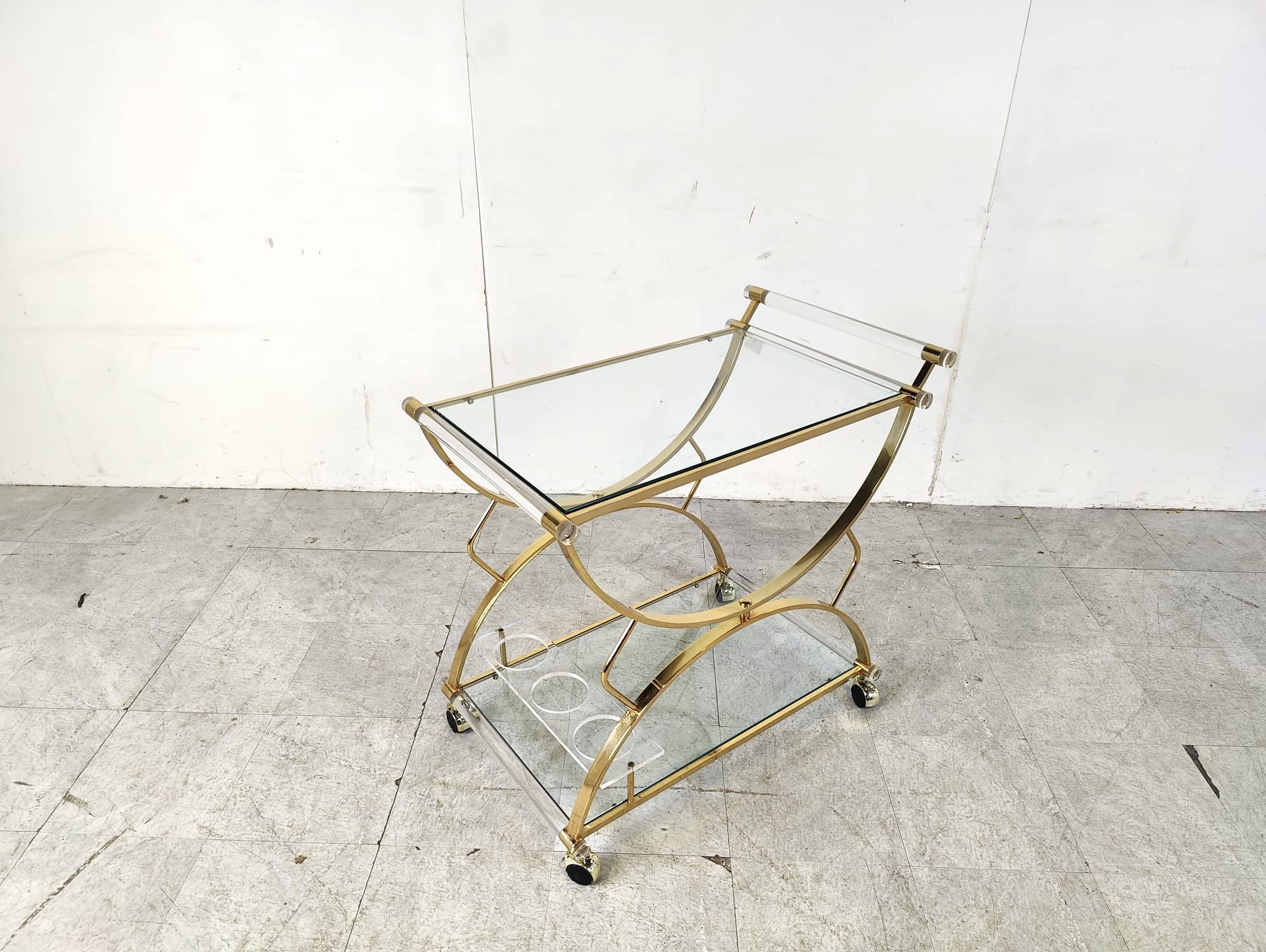 Elegant vintage brass and lucite serving trolley with clear glass tops.

The trolley has a handy integrated bottle holder.

1970s - France

Very good condition

Dimensions:
Height: 78cm
Width: 50cm
Depth: 80cm

Ref.: 415266