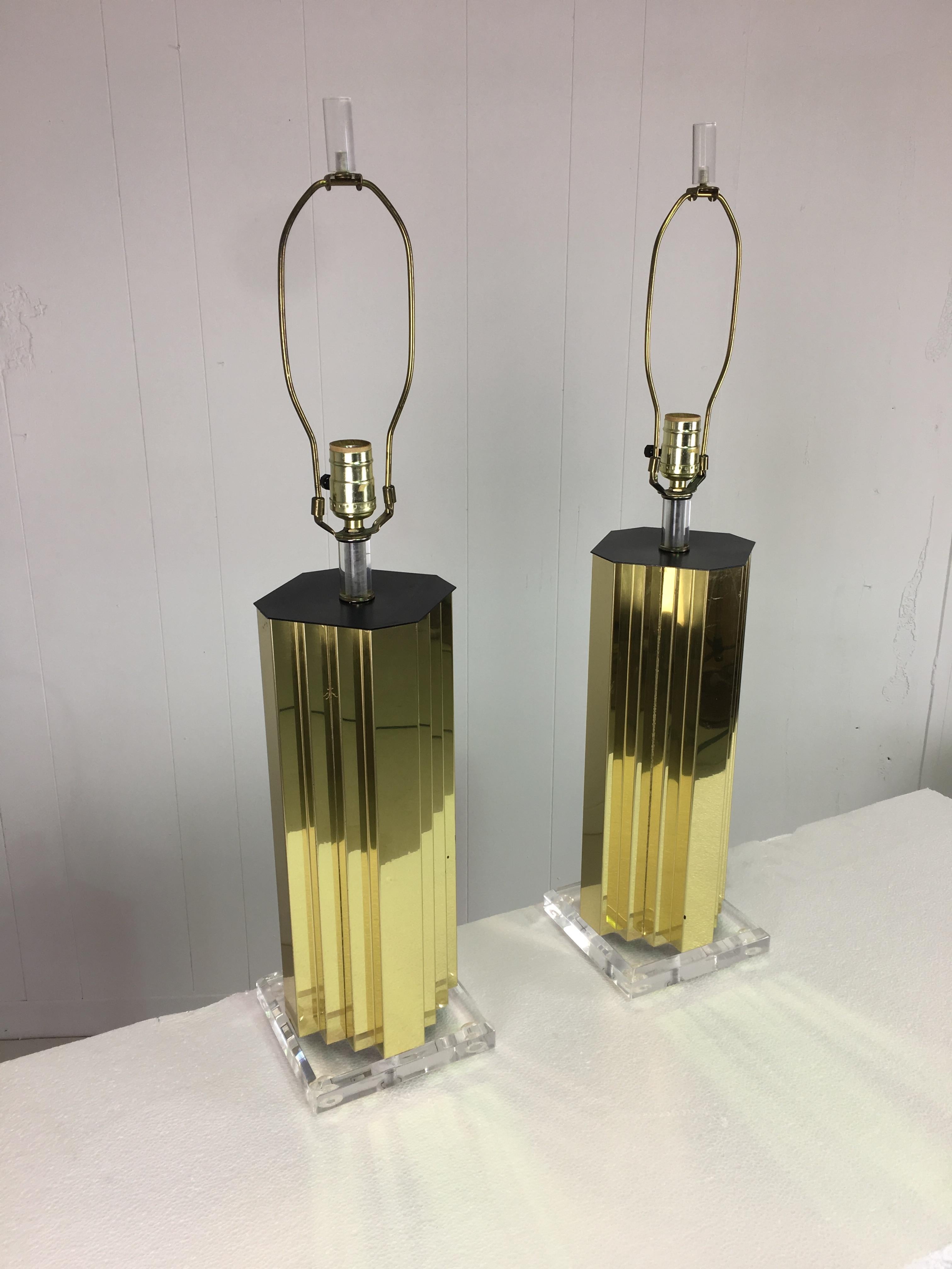 Probably 1980s production as part of the Art Deco Revival period. Skyscraper modernist lamps with Lucite finials, stem to light bulb and bases. In very good condition with only a few spots of oxidation to the brass. The brass is finished on all