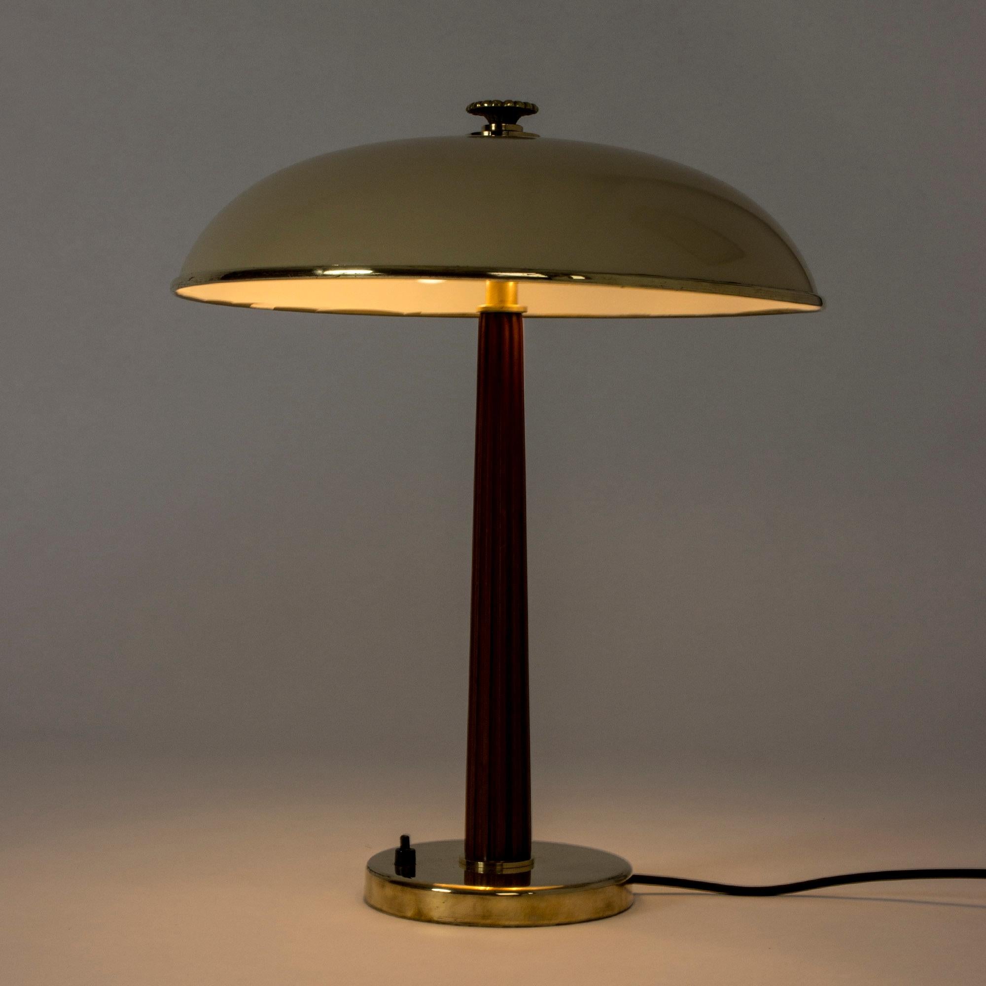 Beautiful table lamp from Böhlmarks, with a brass base, mahogany handle and cream colored lacquered metal shade adorned with a brass flower.
  