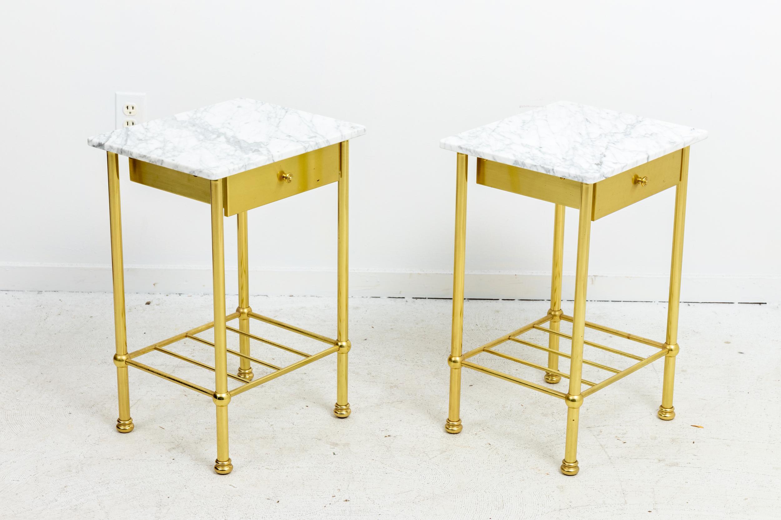 Pair of small side tables with polished brass base and white marble top, circa mid-20th century. The piece also features a single drawer and an open bottom shelf. Please note of wear consistent with age.