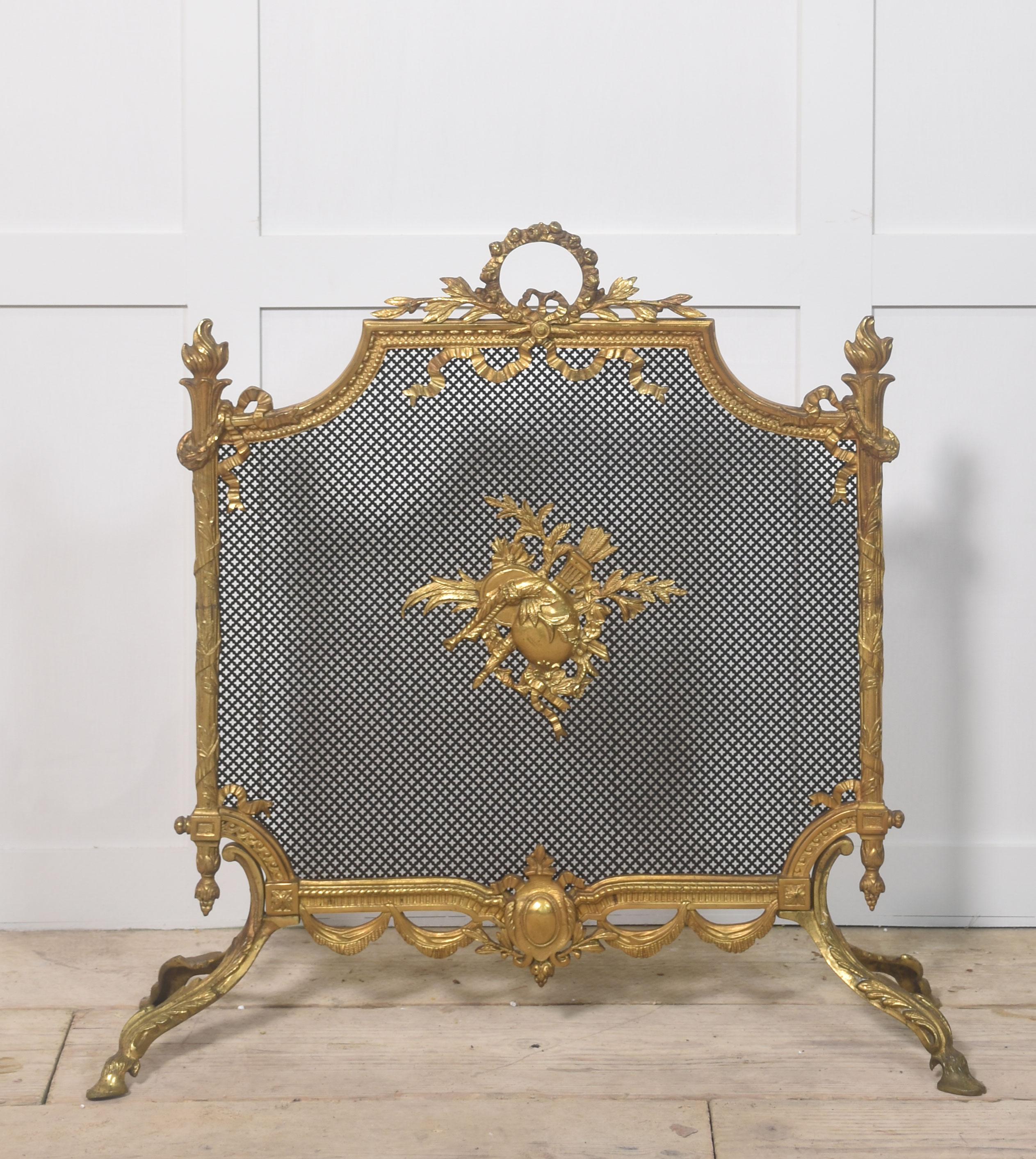 Pantalla de chimenea francesa de latón pulido y malla. El marco rectangular de estilo rococó se compone de volutas y vides detalladas, y el panel de malla con aplique central. El armazón descansa sobre cuatro patas con volutas cuidadosamente