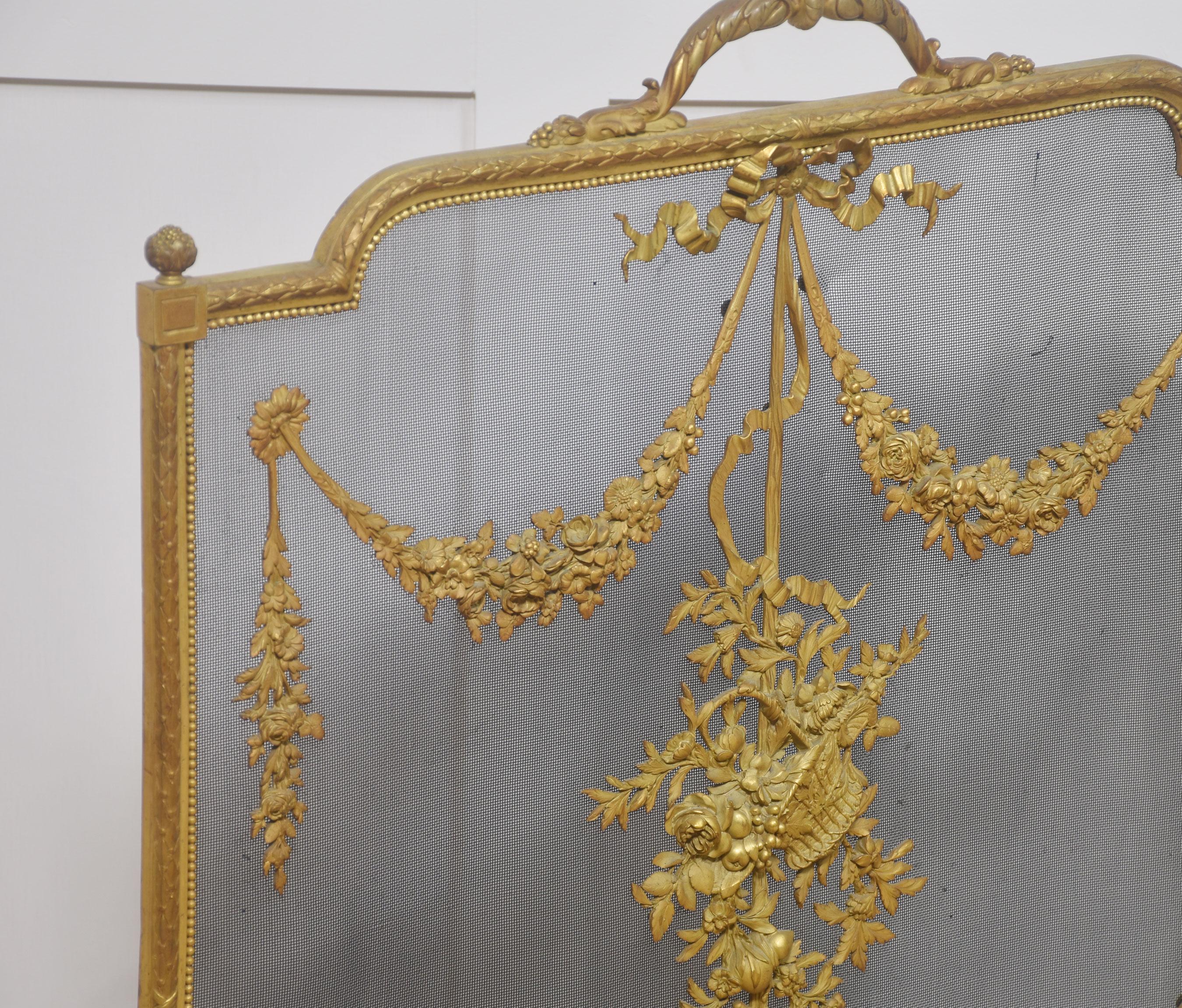 Polished brass and mesh French fire screen. The Rococo-style rectangular frame is composed of detailed scrolls and vines, and the mesh panel with central appliqué. The frame rests on four carefully executed scrolled legs terminating in hoof