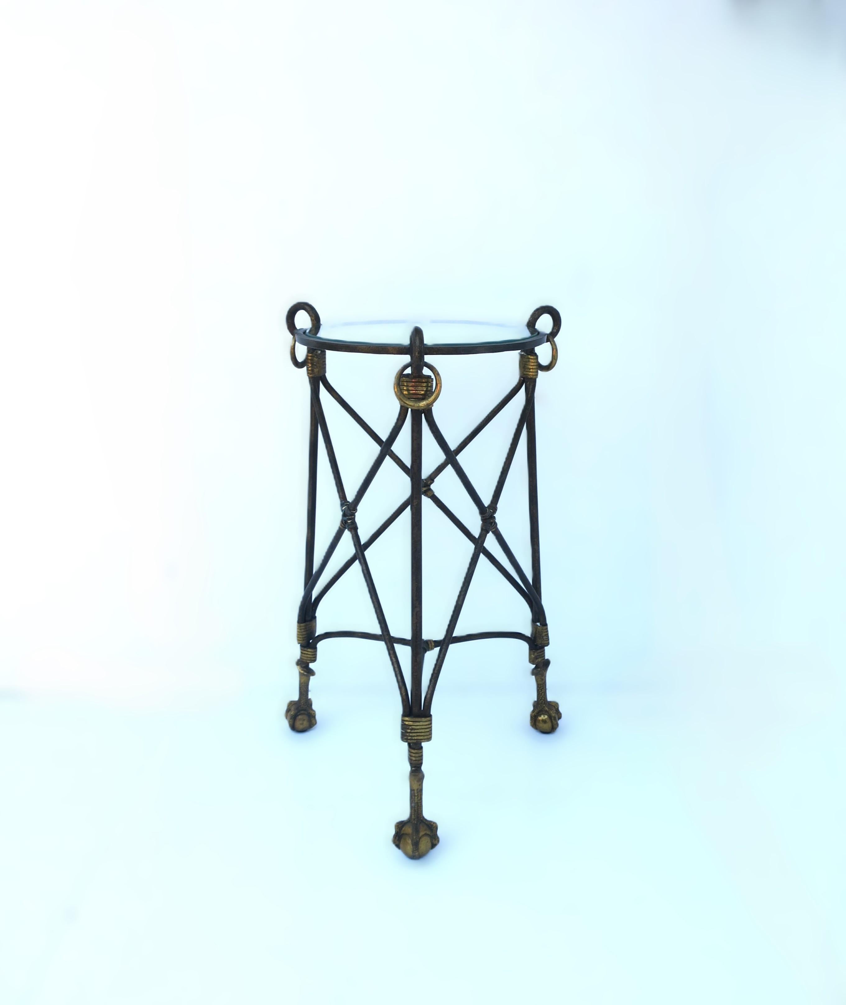 A substantial metal and brass ball and claw drinks table, circa late-20th century. Table is metal with an antiqued finish, round glass top, and brass details: wrapped brass and brass loops around top, brass ball and claw feet with tripod base. A