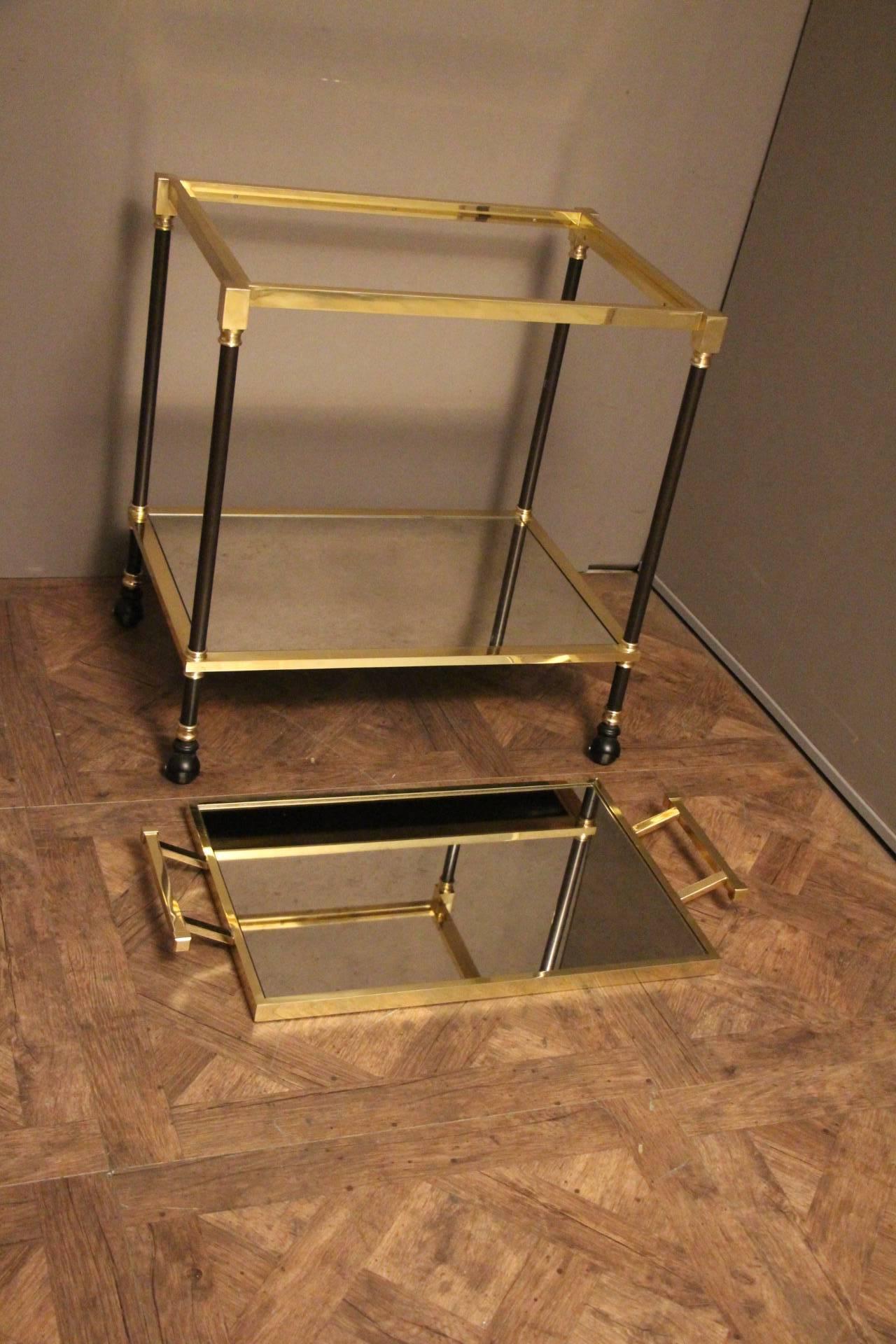 This very elegant and sturdy rolling bar trolley features two framed levels in mirror. The upper framed brass tray with its two side handles is removable.
It is particularly elegant thanks to it is black steel and golden brass legs and its shape is