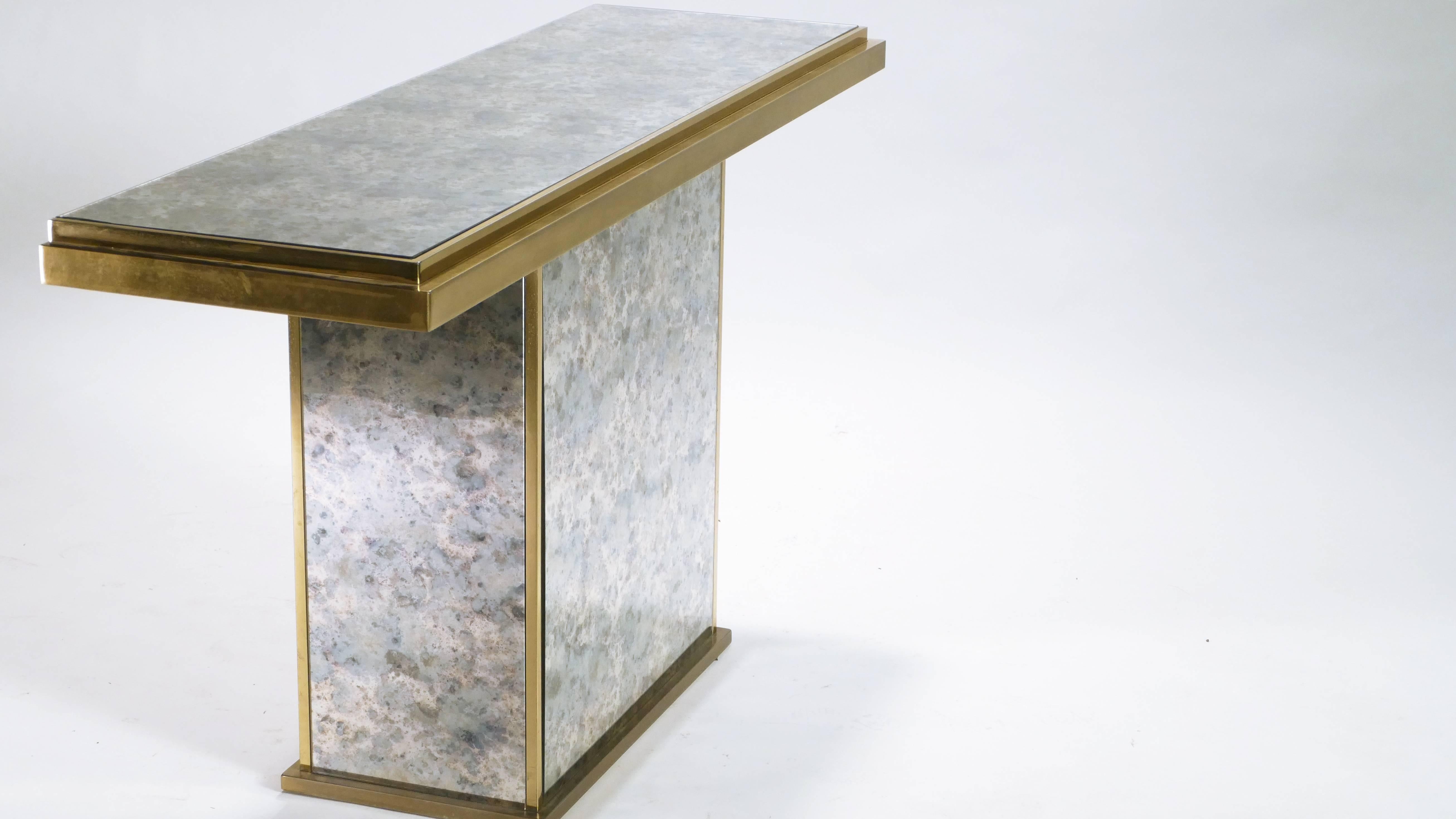 Extravagant brass details and an aged, mirrored surface make this gorgeous midcentury console an example of the Hollywood regency style that championed decorative and decidedly luxurious design. Its neutral, dappled color and strong, simple