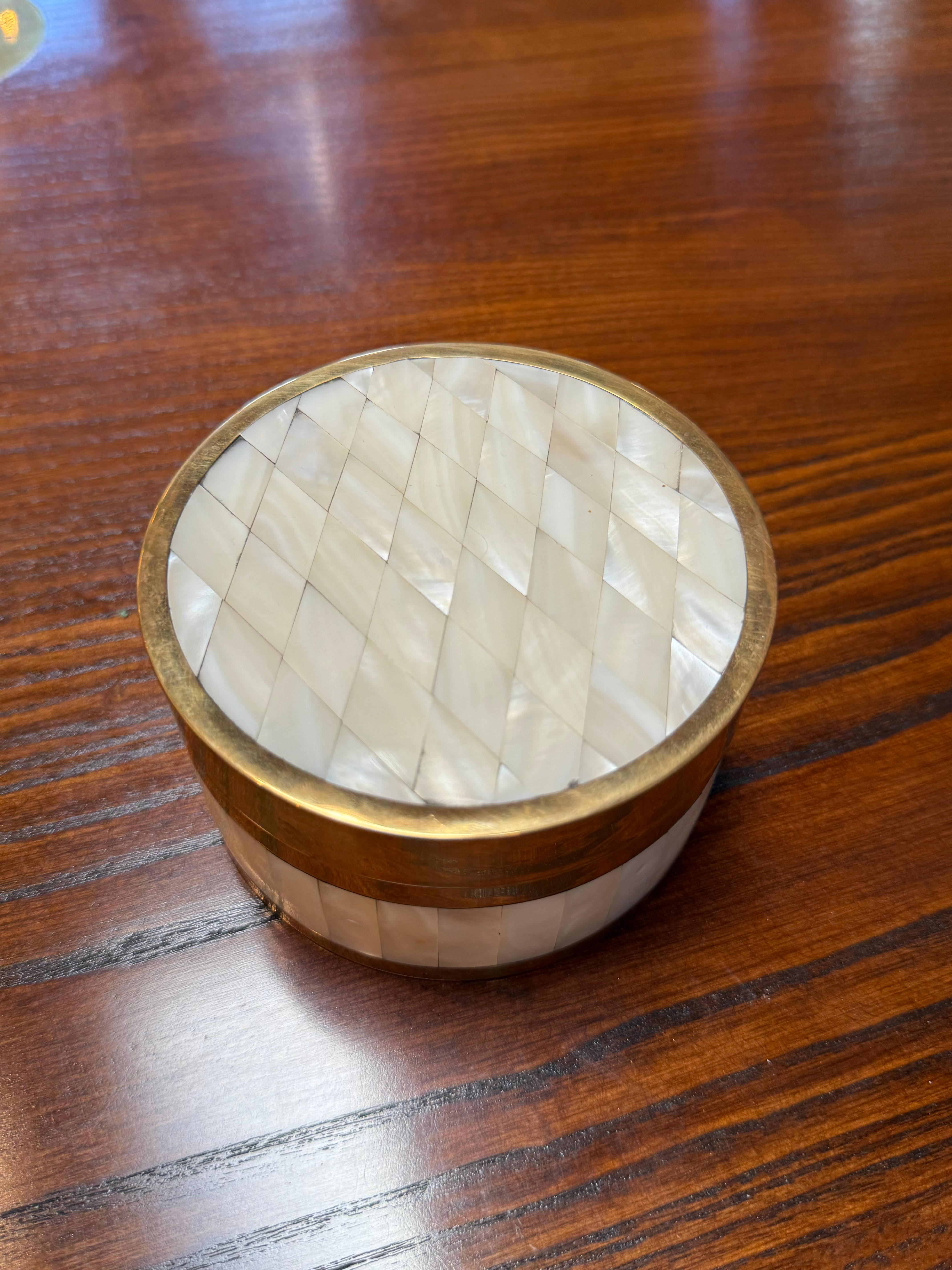 Elegant round decorative box featuring a brass frame with intricate mother-of-pearl inlay arranged in a diamond pattern across the lid and sides. The luminous iridescence of the shell contrasts beautifully with the warm brass tones, creating a