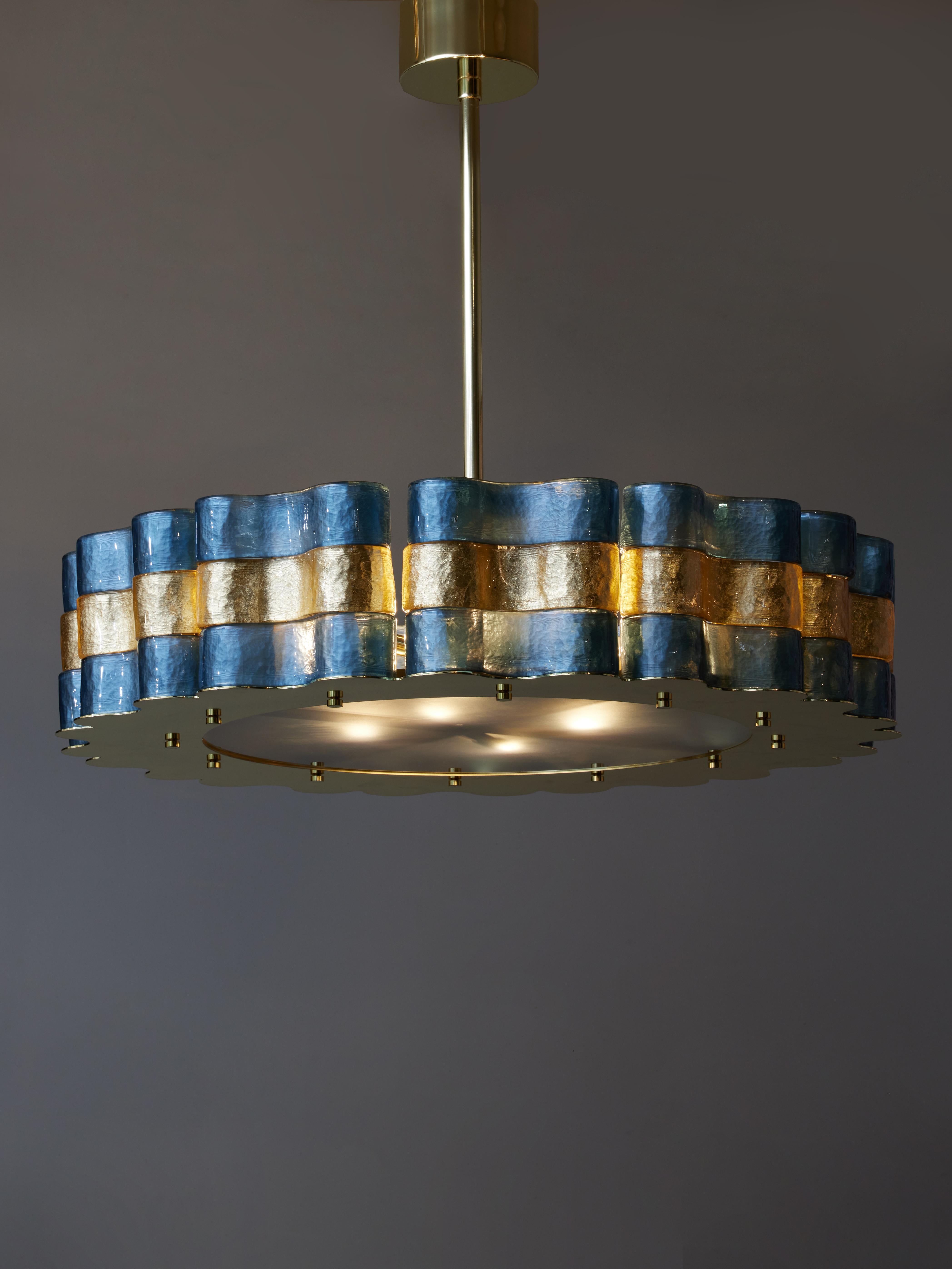 Round chandelier made of a brass structure on which are placed wavy pieces of Murano glass, alternating between gold and dark blue.