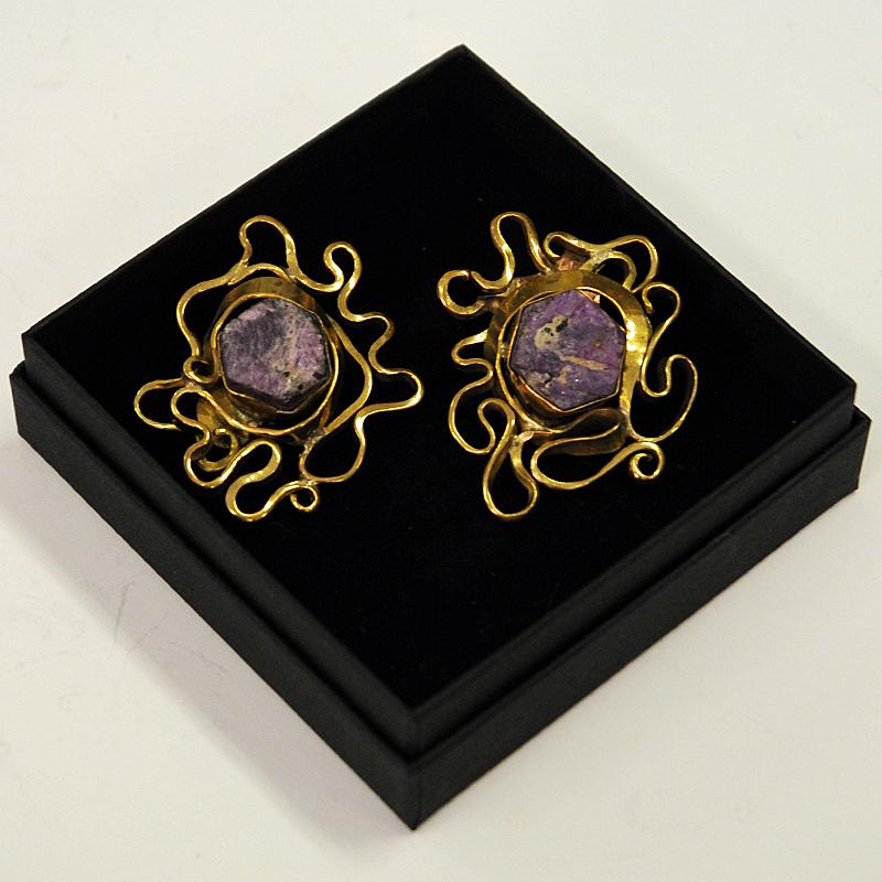 Gorgeous midcentury brass clip earrings with a purple nature stone by designer Anna Greta Eker, Norway, 1970s. Organic and oval shape with brass ornaments. A typical couple of vintage earrings reflecting some of the best work within design and